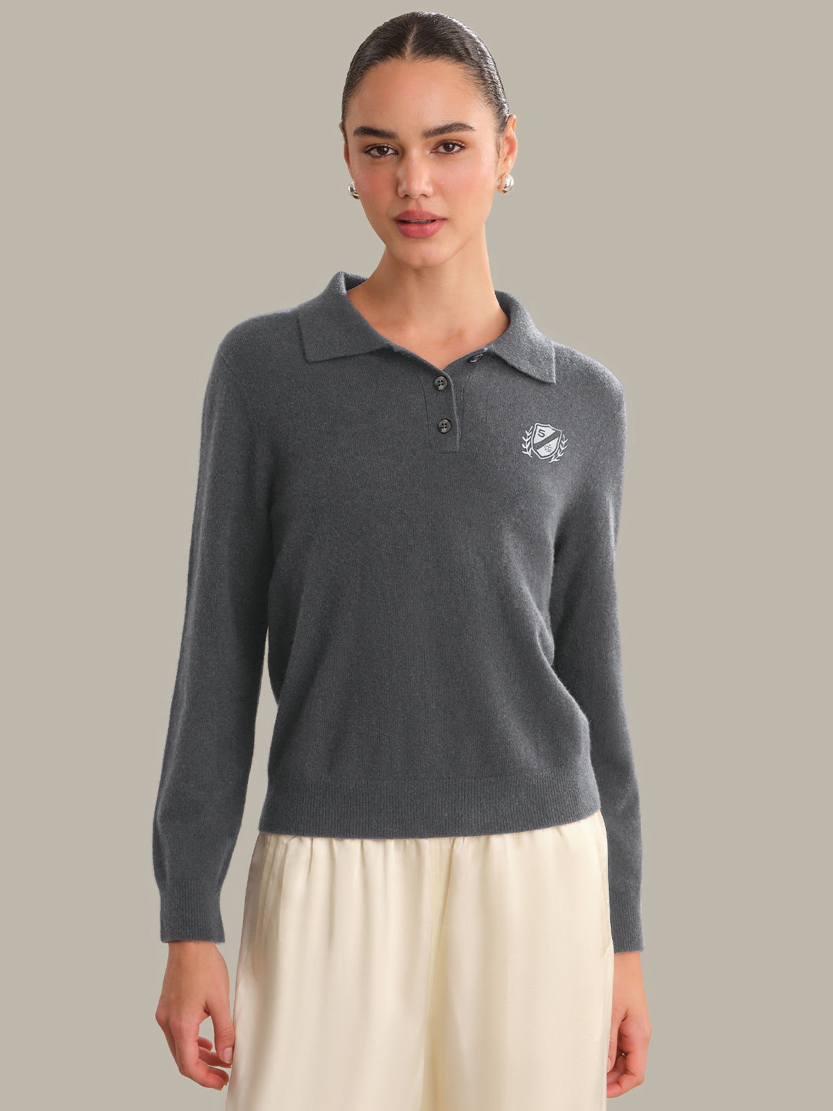 Woman wearing a gray sweater with a logo on a plain background