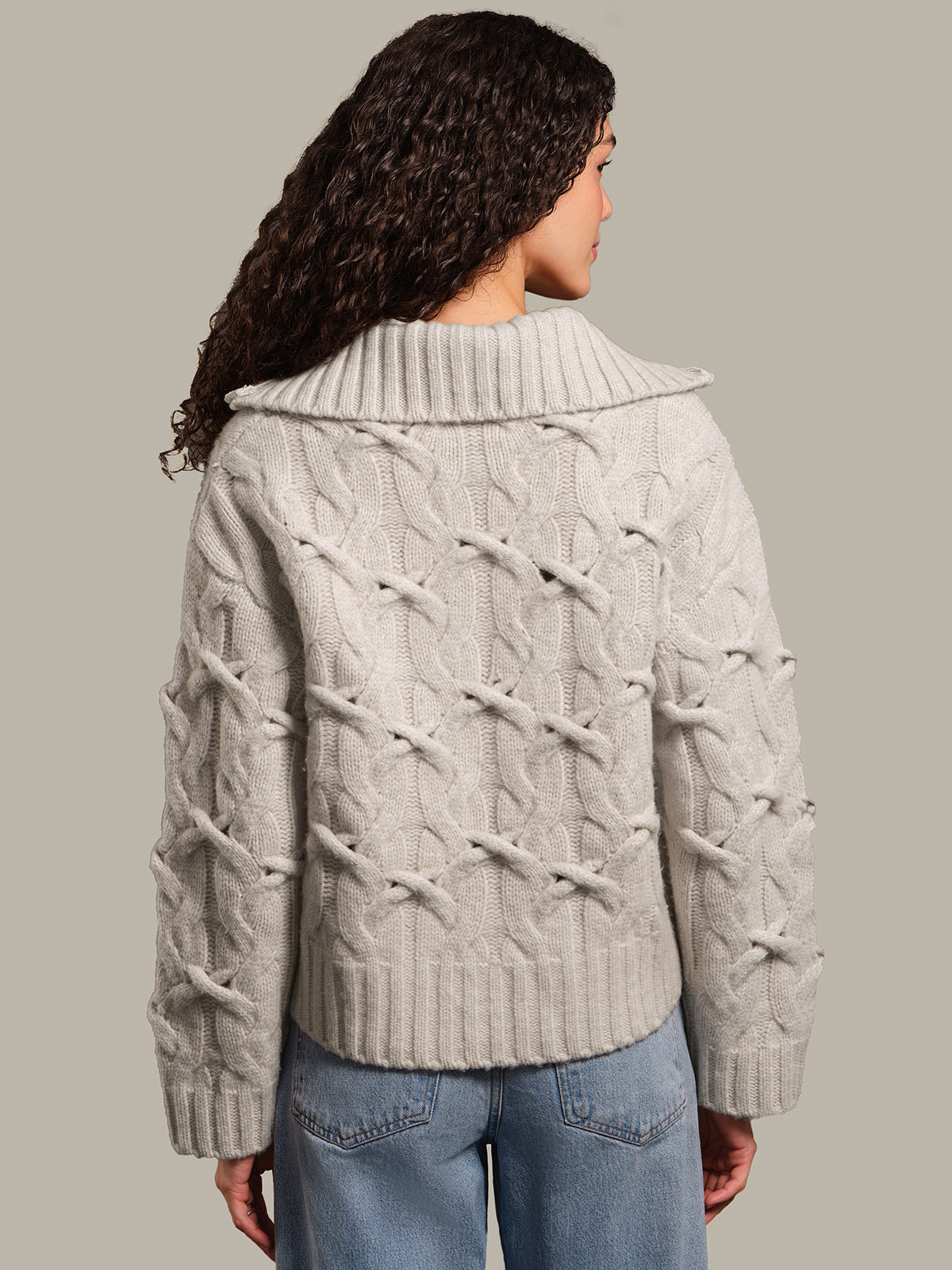 Person wearing a light gray cable knit sweater against a neutral background