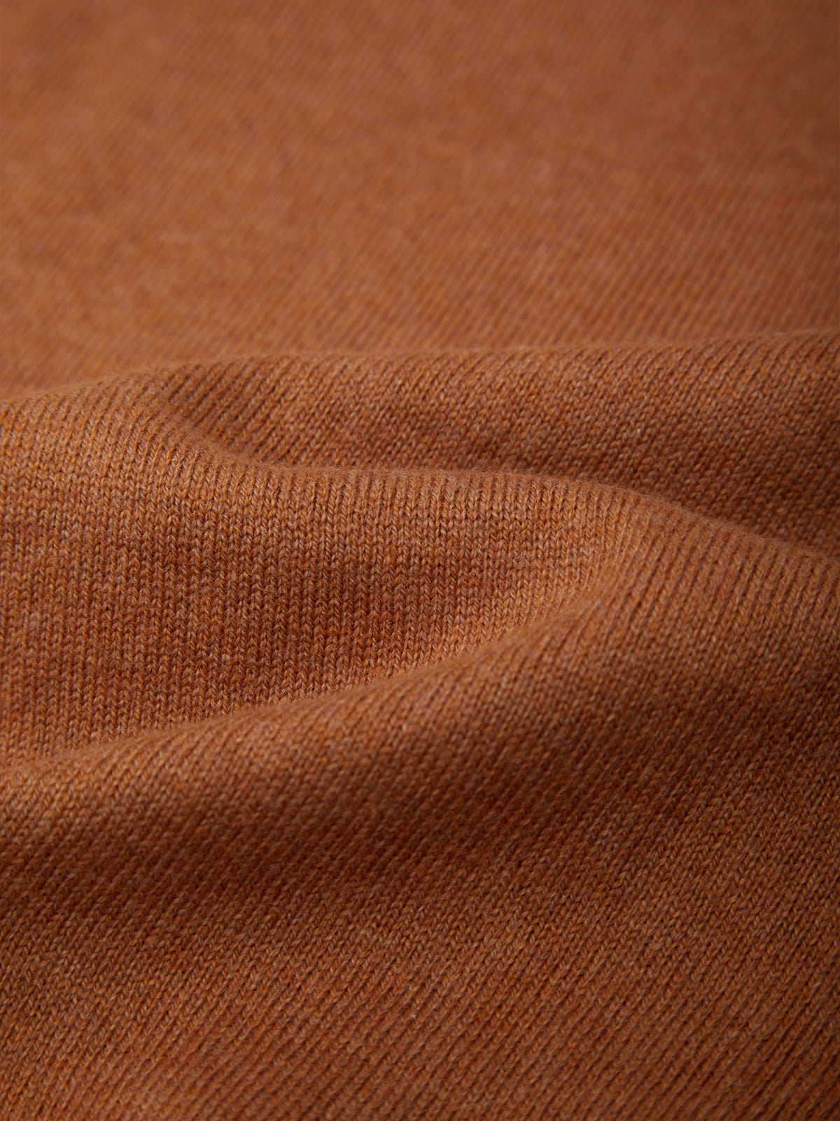 Close-up of a ribbed knit fabric in a warm rust or terracotta brown color, showing the texture and drape of the material.