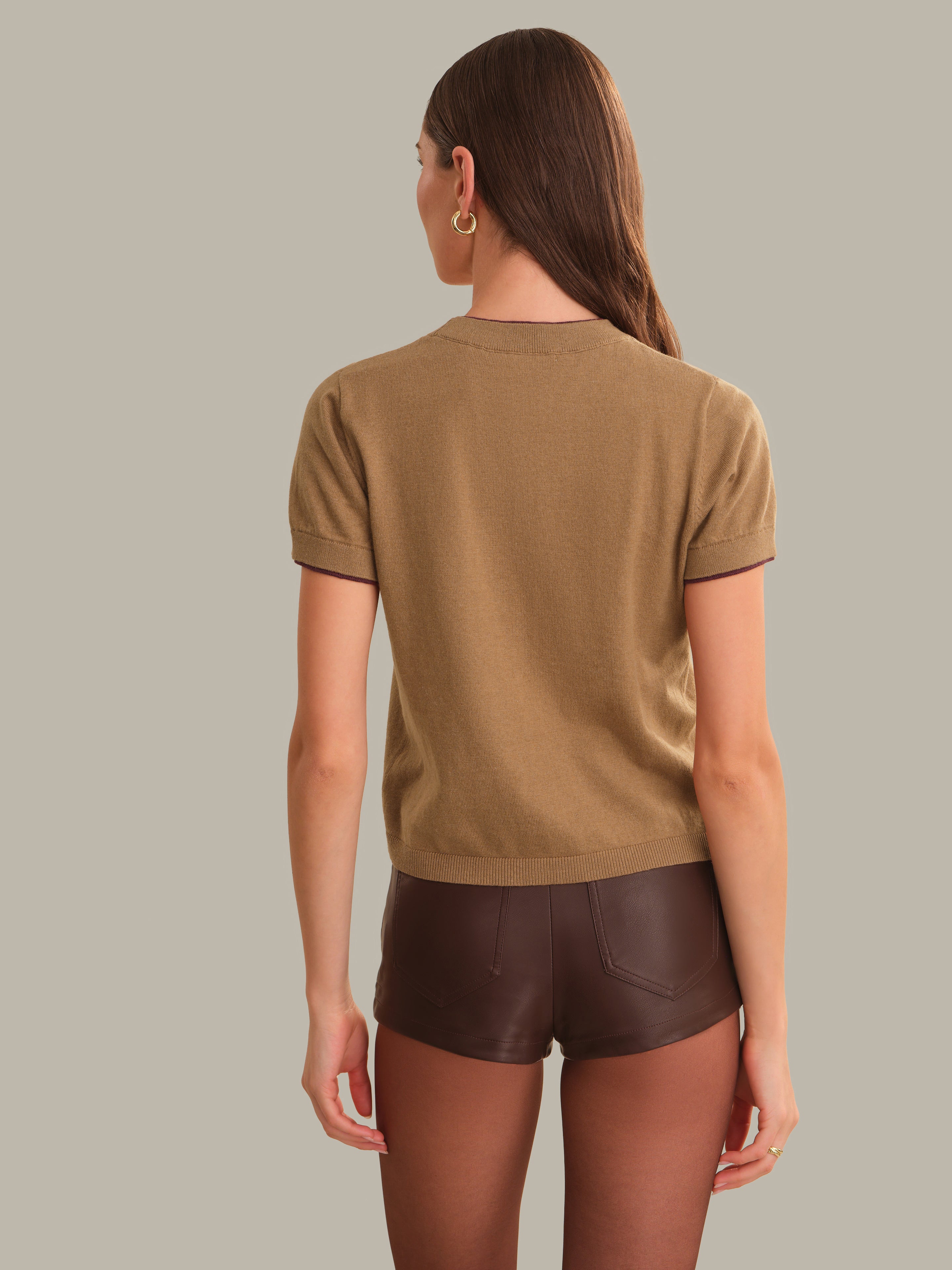 A woman shown from the back wearing a short-sleeve knit top in camel brown and dark brown shorts, set against a solid light gray background.