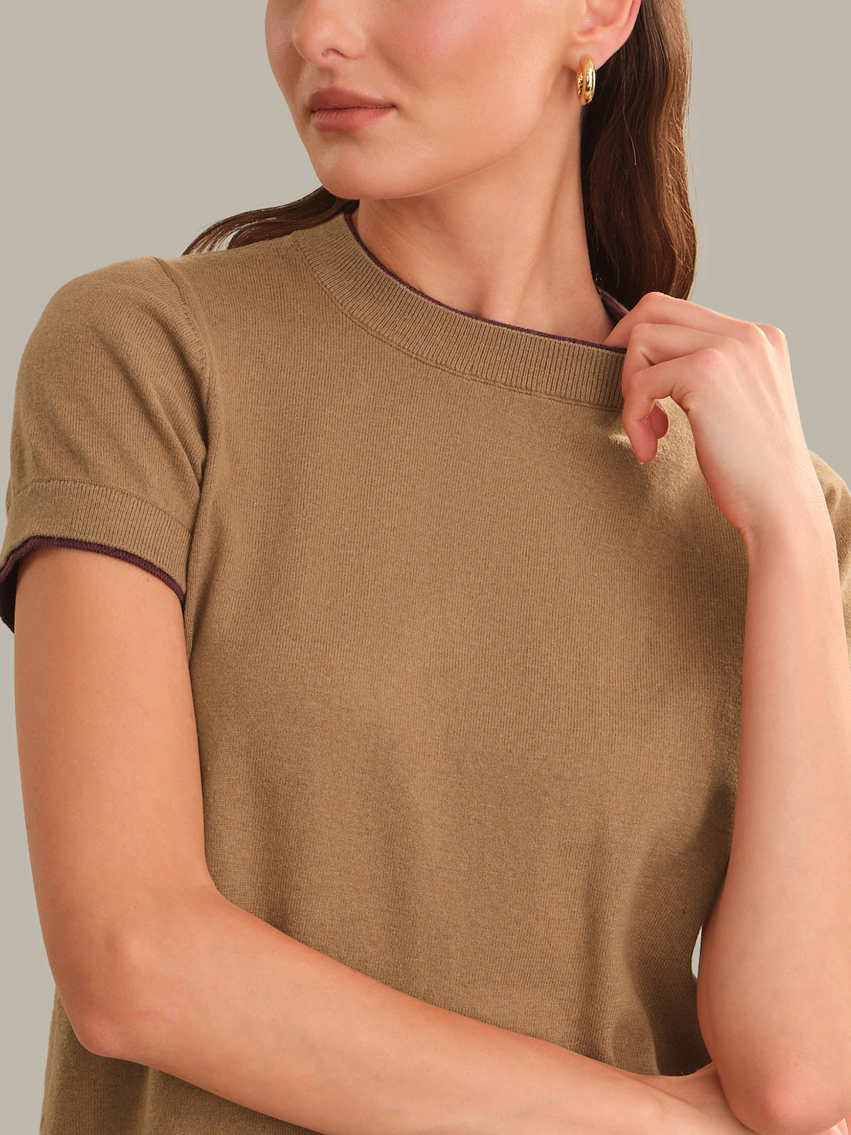 A close-up of a woman wearing a short-sleeve crewneck knit top in camel brown, showing the ribbed collar and sleeve cuffs.