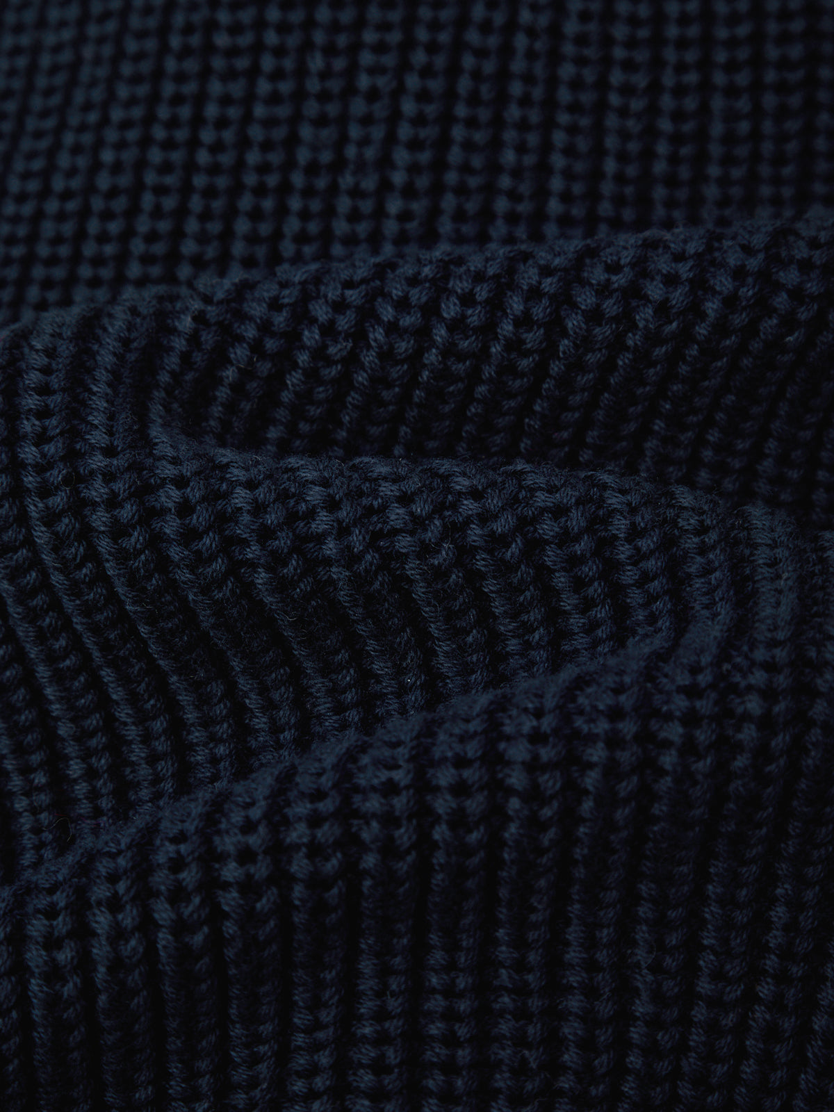 Close-up of a dark navy blue ribbed knit fabric texture with soft folds.