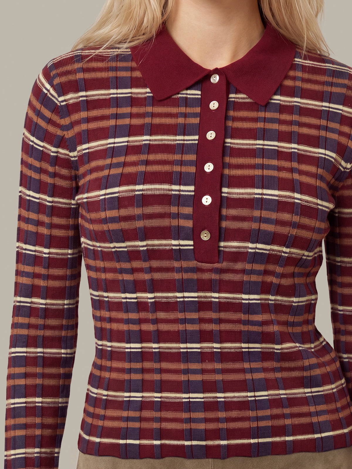 A close-up of a woman wearing a long-sleeve plaid polo shirt with a solid burgundy collar and button placket. The shirt features a red, navy blue, and beige plaid pattern.