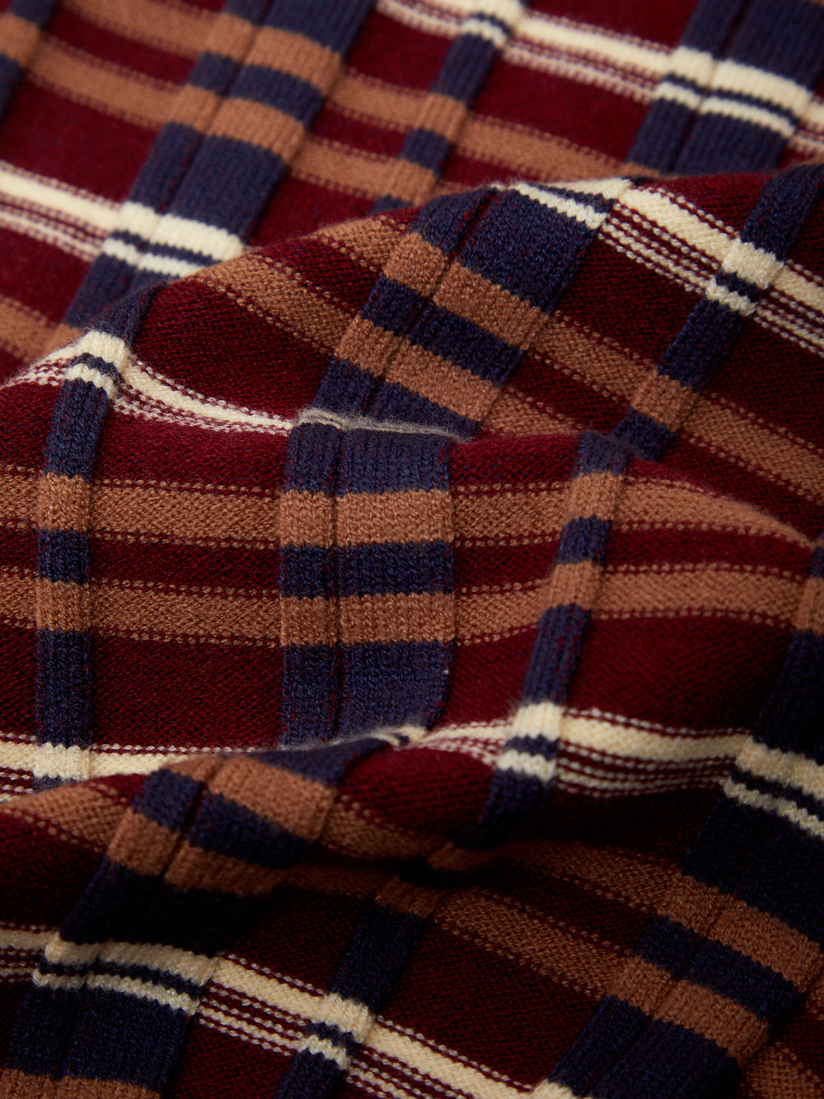 A close-up of a plaid fabric with a tartan pattern in deep red, navy blue, tan, and white, showing the woven texture and soft folds.