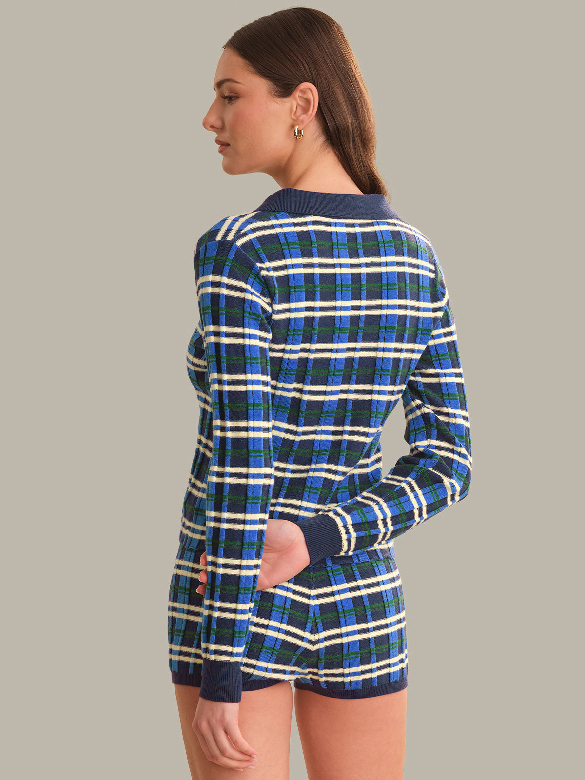 A woman shown from the back wearing a blue, green, and white plaid long-sleeve top and matching shorts against a solid gray background.