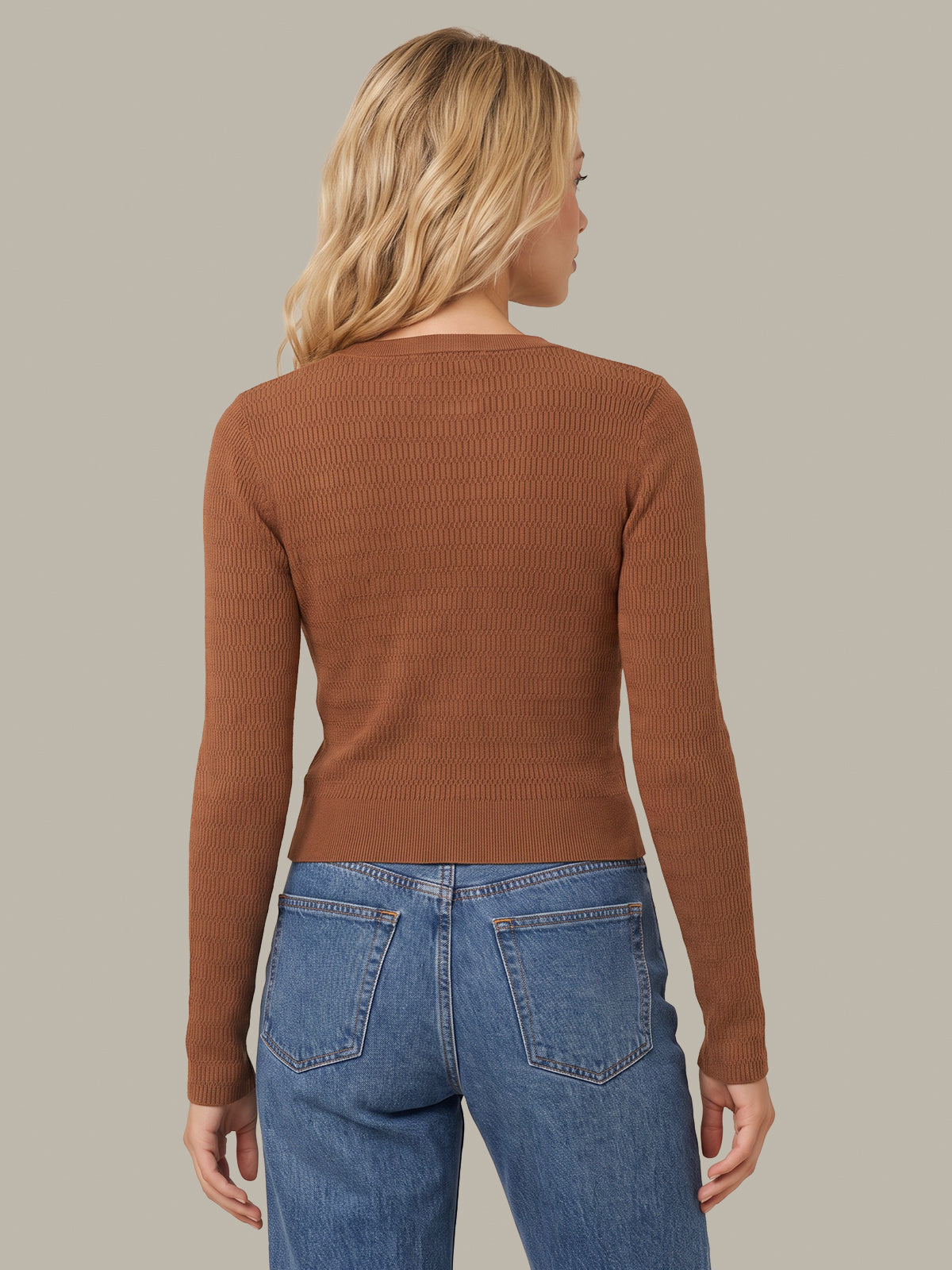 A woman shown from the back wearing a fitted ribbed long-sleeve knit top in a warm rust brown color, paired with blue jeans, against a solid light gray background.