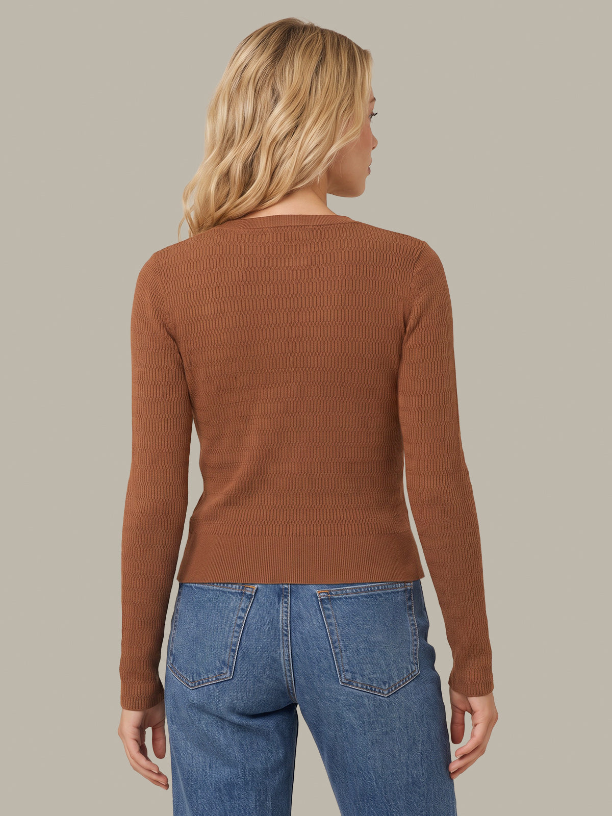 A woman shown from the back wearing a fitted ribbed knit long-sleeve sweater in a warm rust brown color, paired with blue jeans, against a solid light gray background.