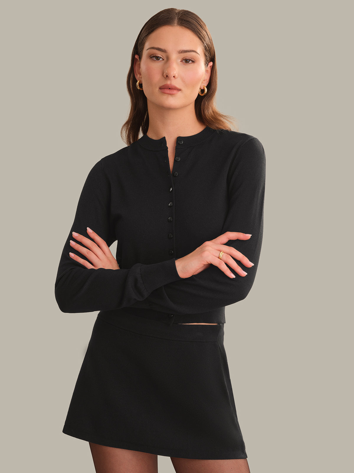 Woman wearing a black long-sleeve top and skirt against a neutral background
