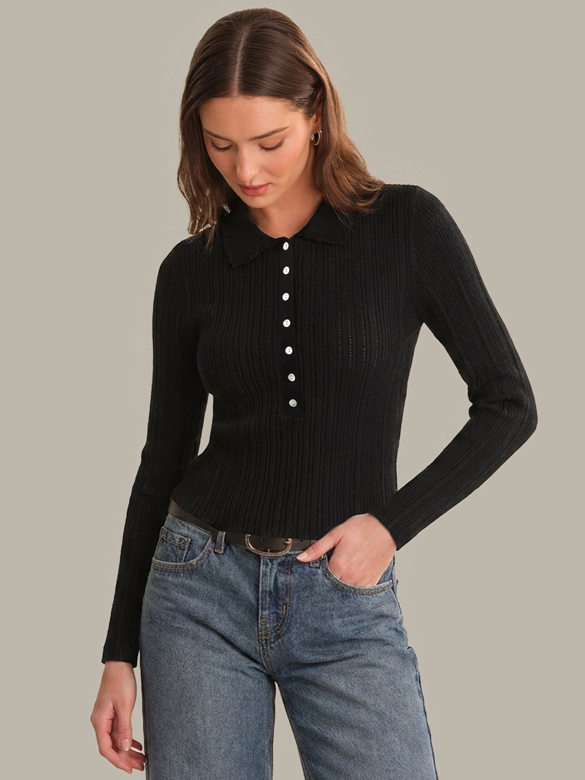 Woman wearing a black ribbed sweater with white buttons and blue jeans on a gray background