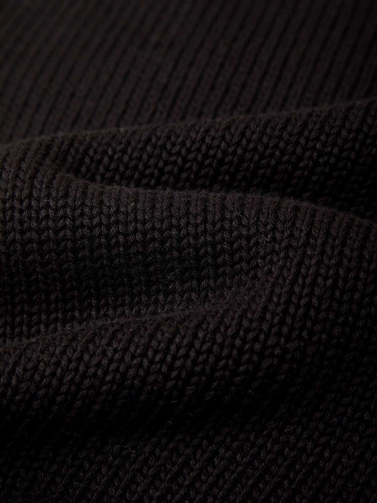 Close-up of a dark knit fabric texture with visible ribbed stitching and soft folds.