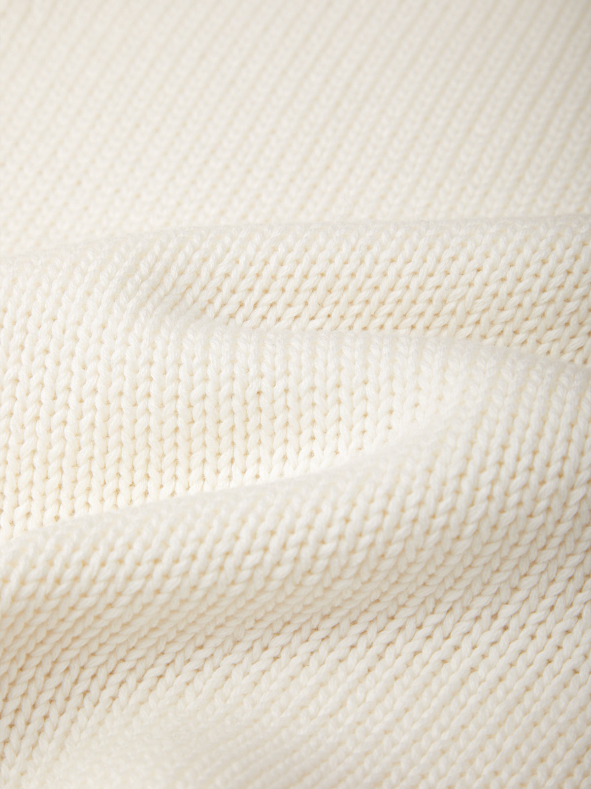 Close-up of a cream-colored knit fabric with a fine ribbed texture and soft folds.