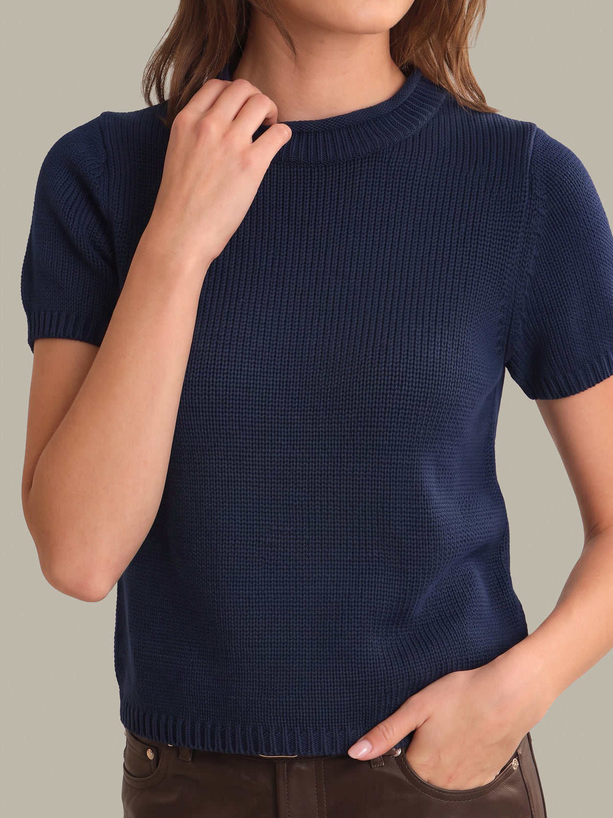 A woman wearing a navy blue short-sleeve ribbed knit sweater, shown from the neck down against a solid light gray background.