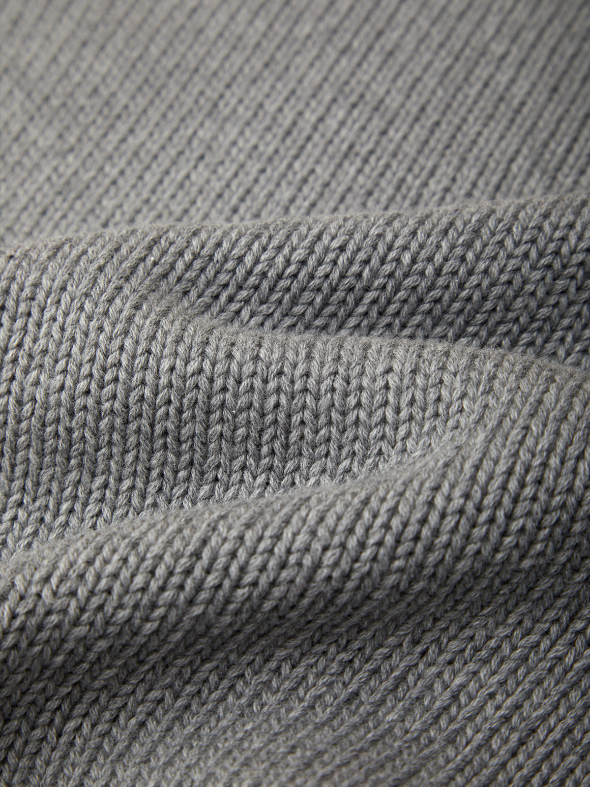 Close-up of a gray knitted fabric texture with soft folds showing the ribbed knit pattern.