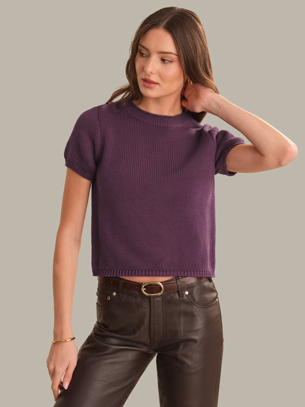 Woman wearing a purple sweater and dark pants on a gray background