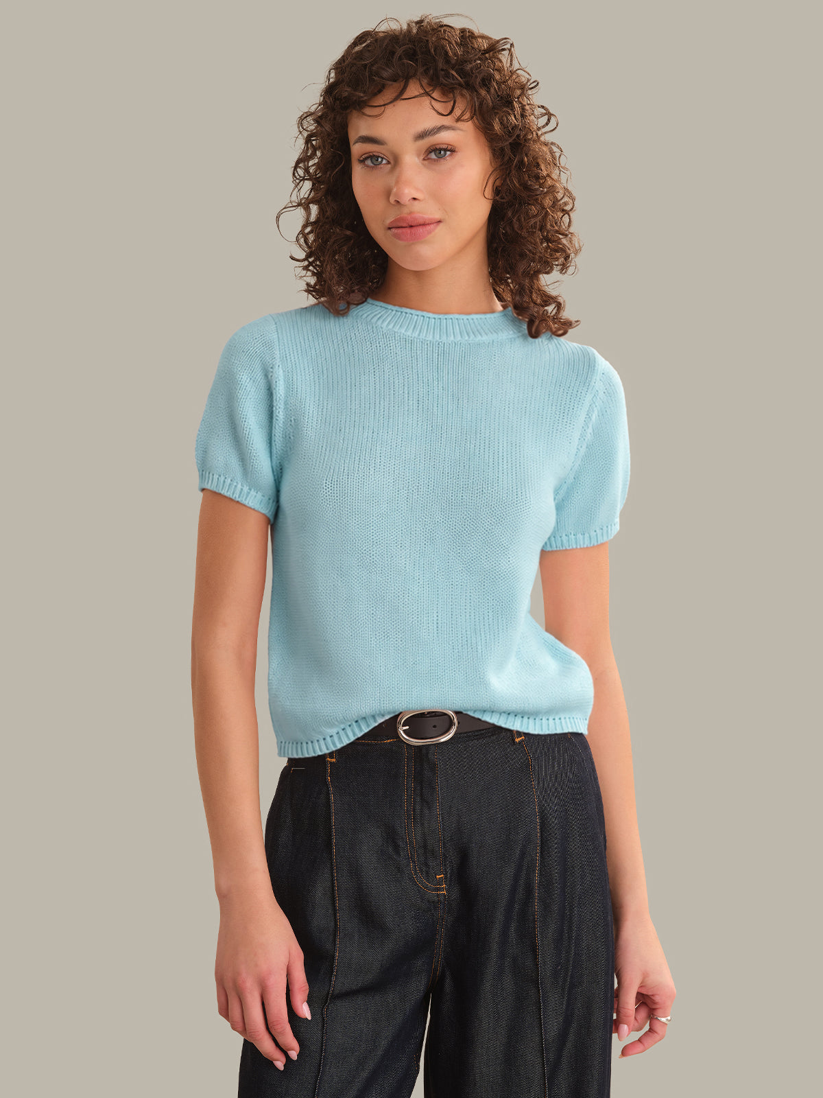 Woman wearing a light blue sweater and dark jeans against a neutral background