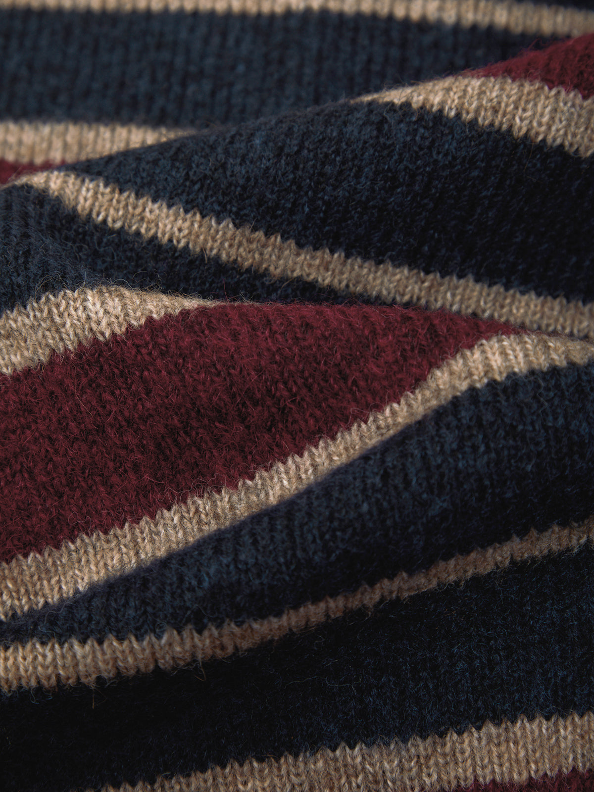 Close-up of a knitted fabric with horizontal stripes in navy blue, burgundy red, and beige.