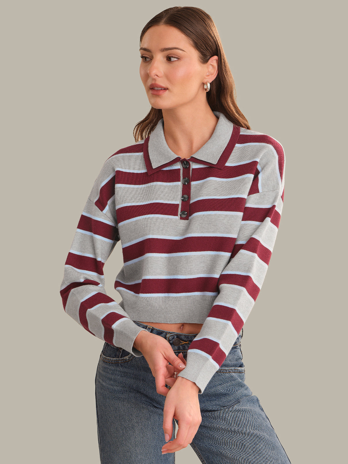 A woman modeling a cropped long-sleeve polo shirt with horizontal maroon and heather gray stripes, paired with blue jeans, against a solid light gray background.