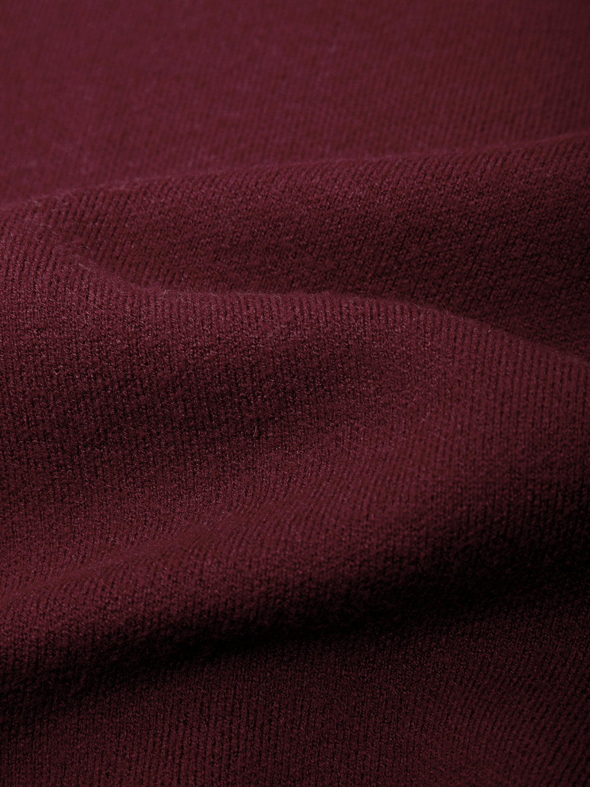 A close-up of draped burgundy knit fabric showing its fine ribbed texture and soft folds.