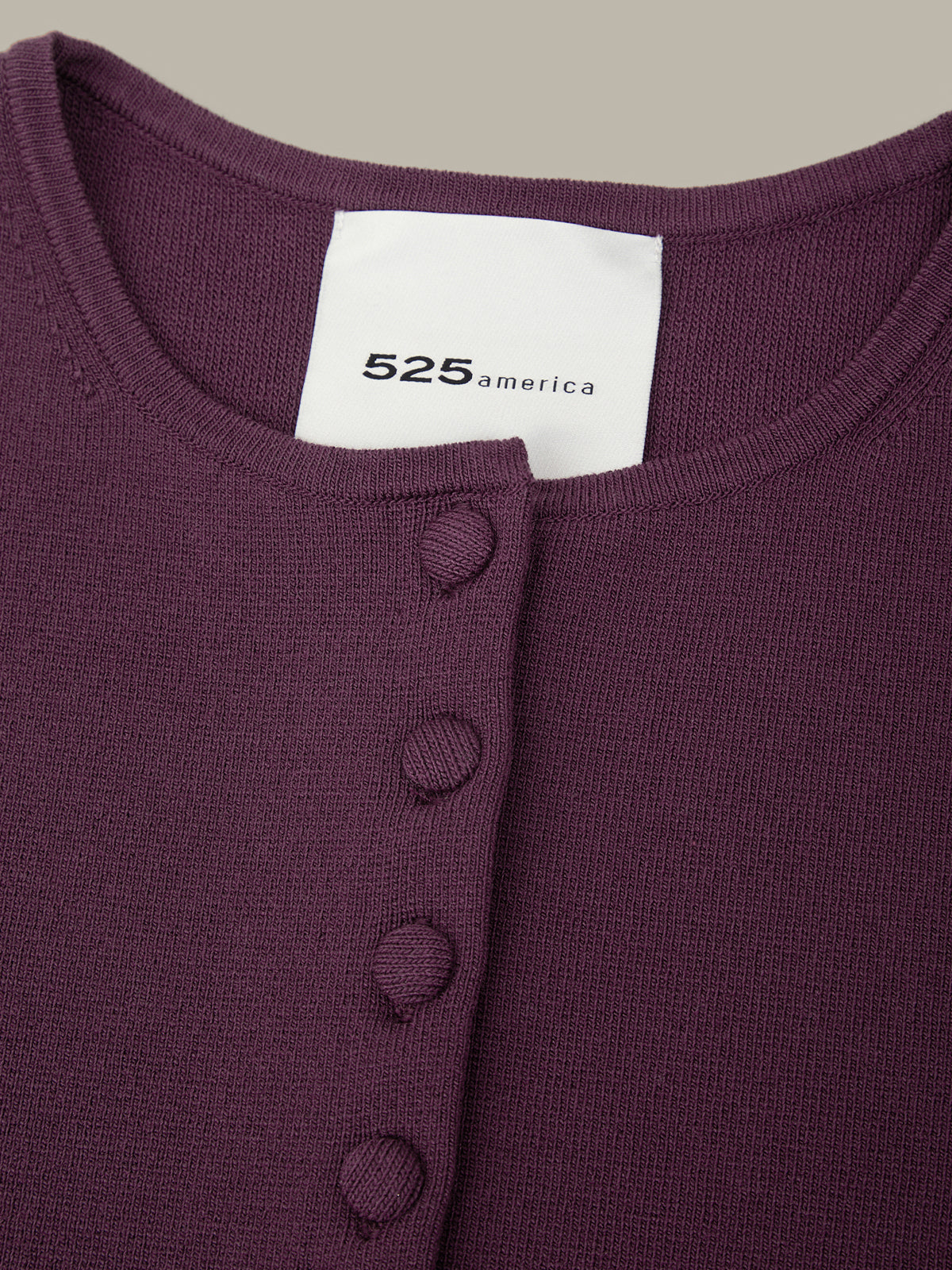Close-up of a purple garment with a visible brand label on a neutral background
