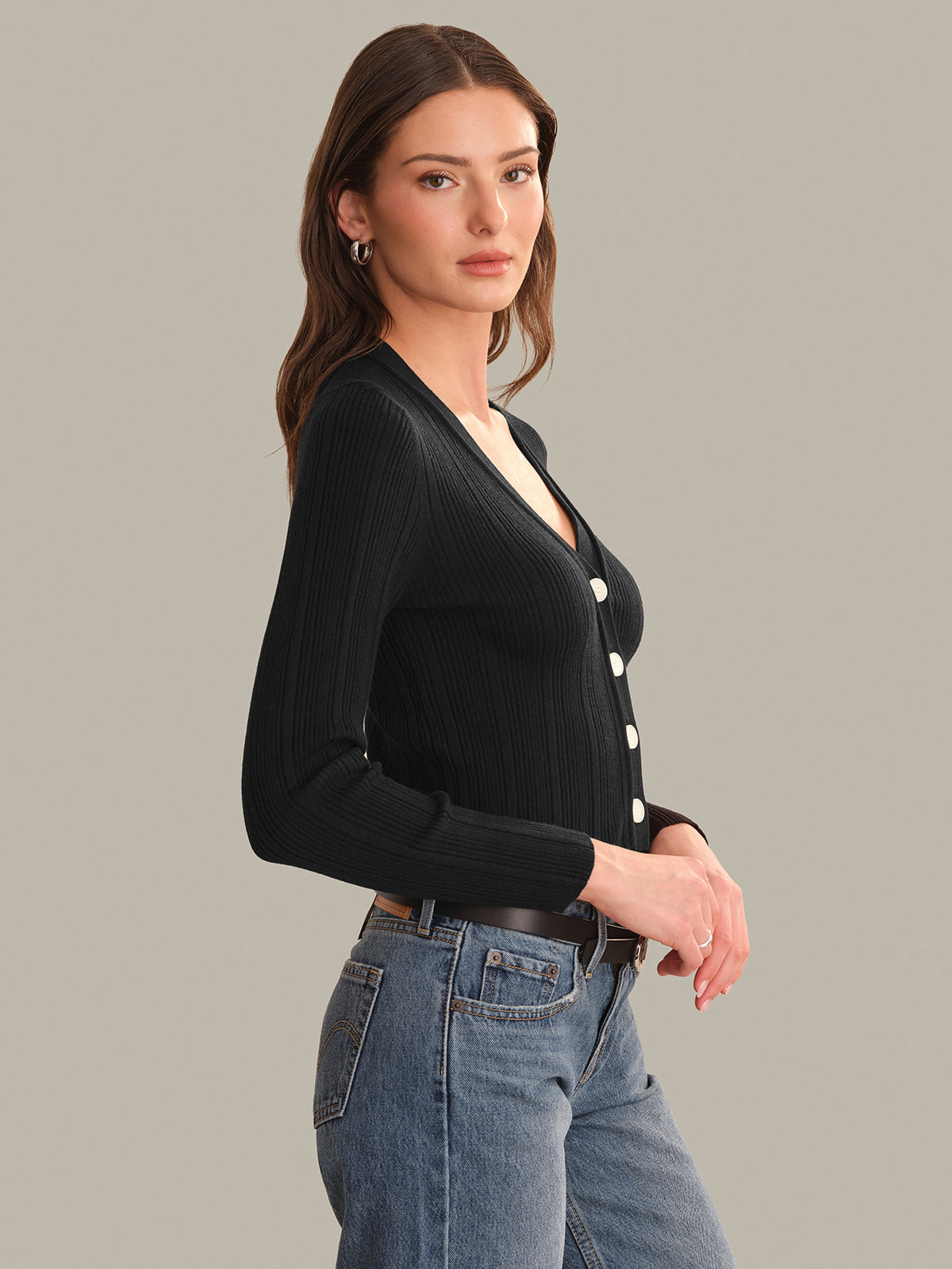 Woman wearing a black cardigan with white buttons, standing against a gray background