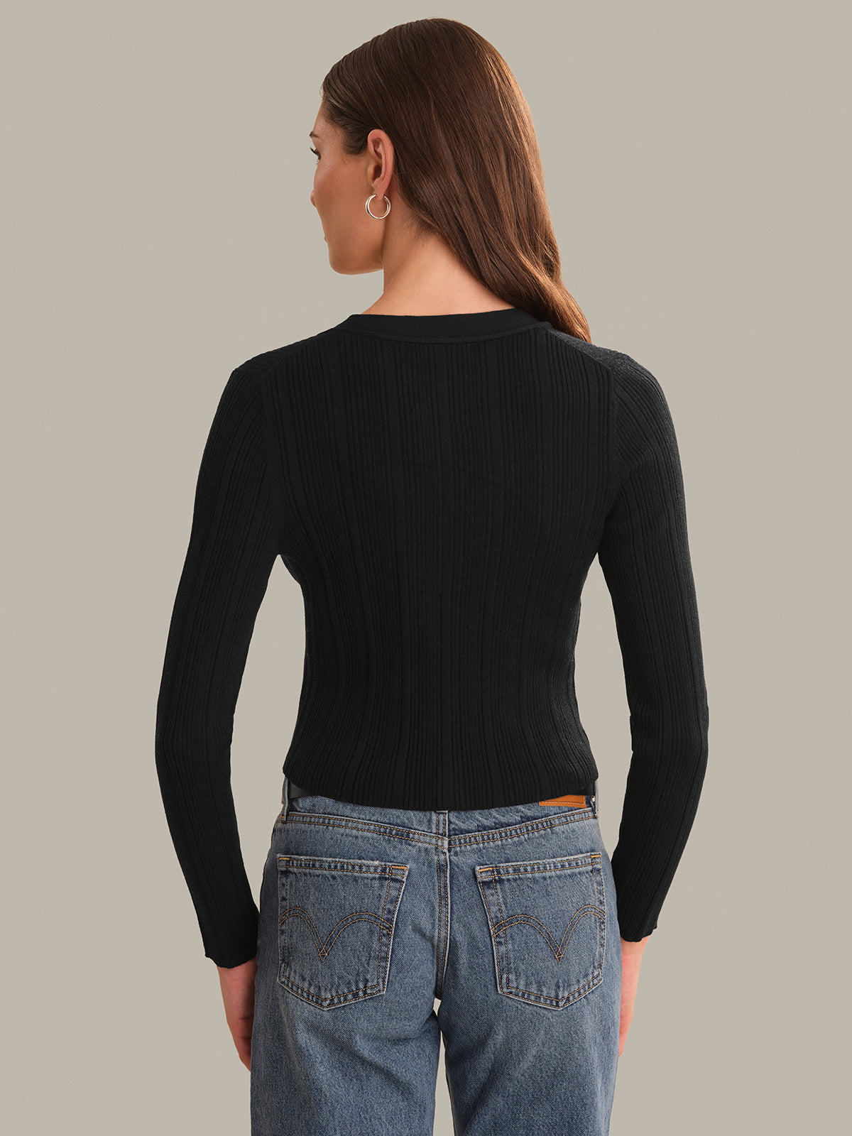 Person wearing a black long-sleeve top and blue jeans on a plain background