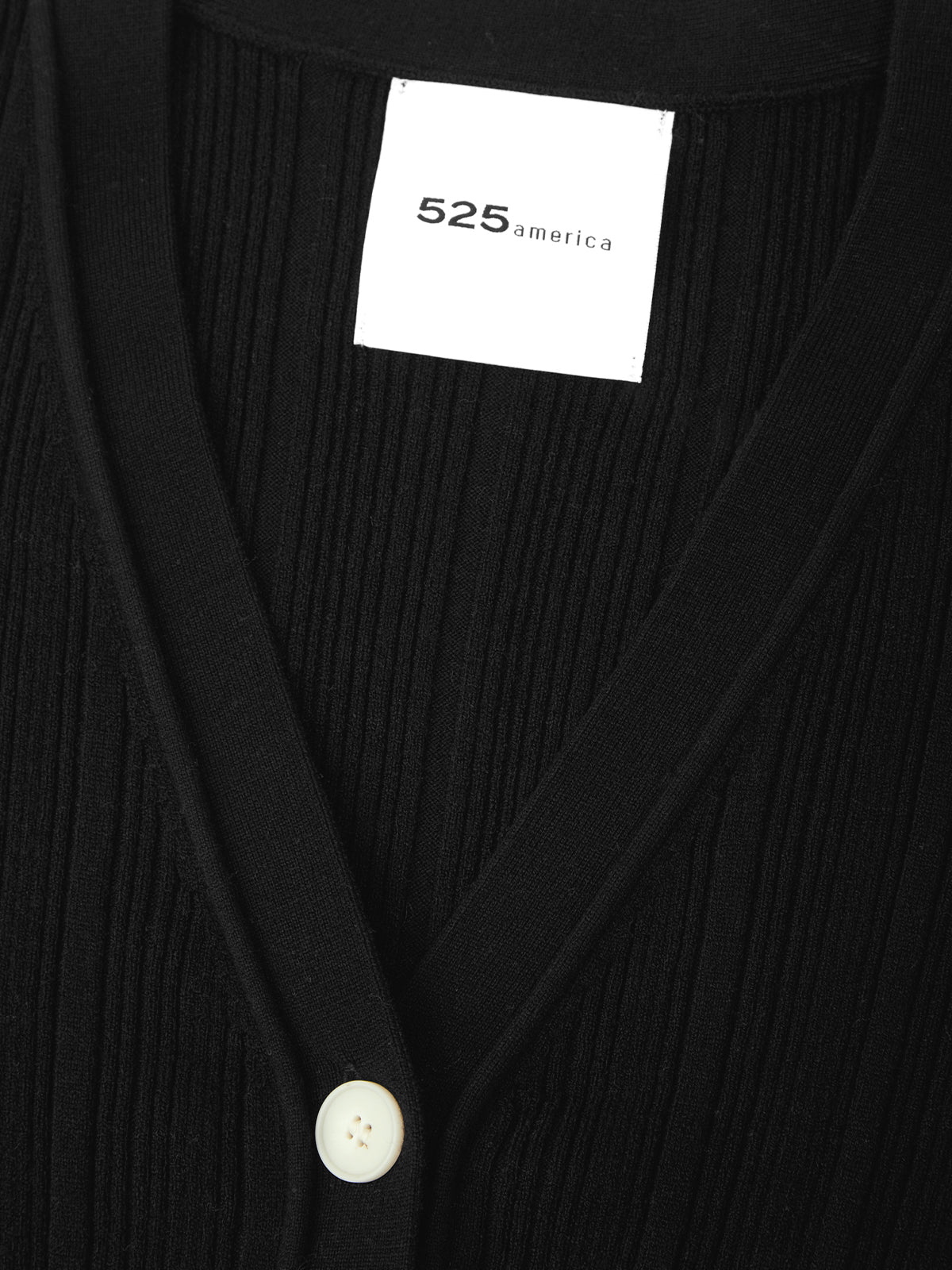 Black ribbed cardigan with a visible brand label on a dark background