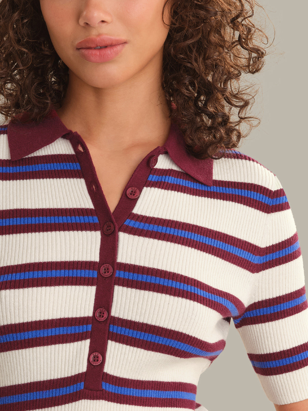 Close-up of a woman wearing a ribbed short-sleeve polo top with horizontal white, burgundy, and blue stripes, featuring a burgundy collar and button placket.