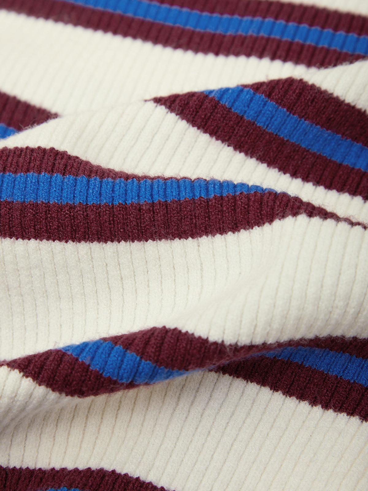 Close-up of a ribbed knit fabric with diagonal stripes in burgundy, cream, and bright blue.