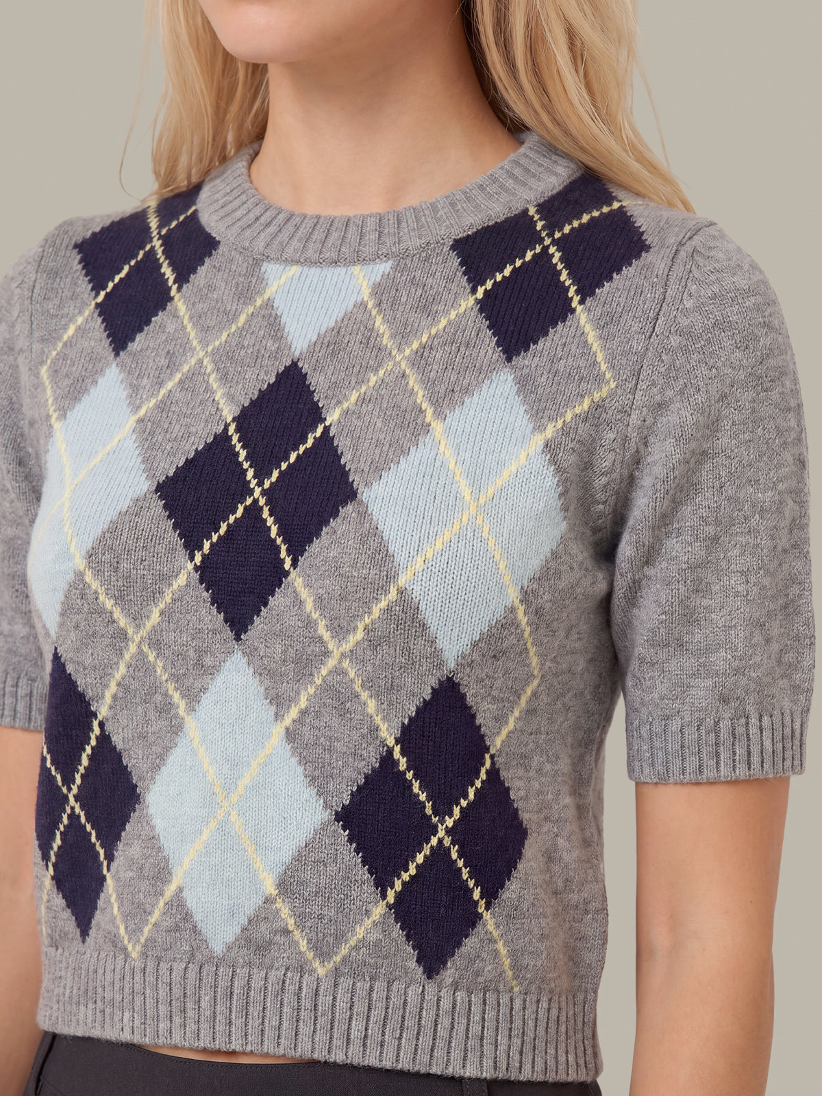 A close-up of a woman wearing a short-sleeve knit sweater with an argyle pattern in gray, navy, pale blue, and cream.