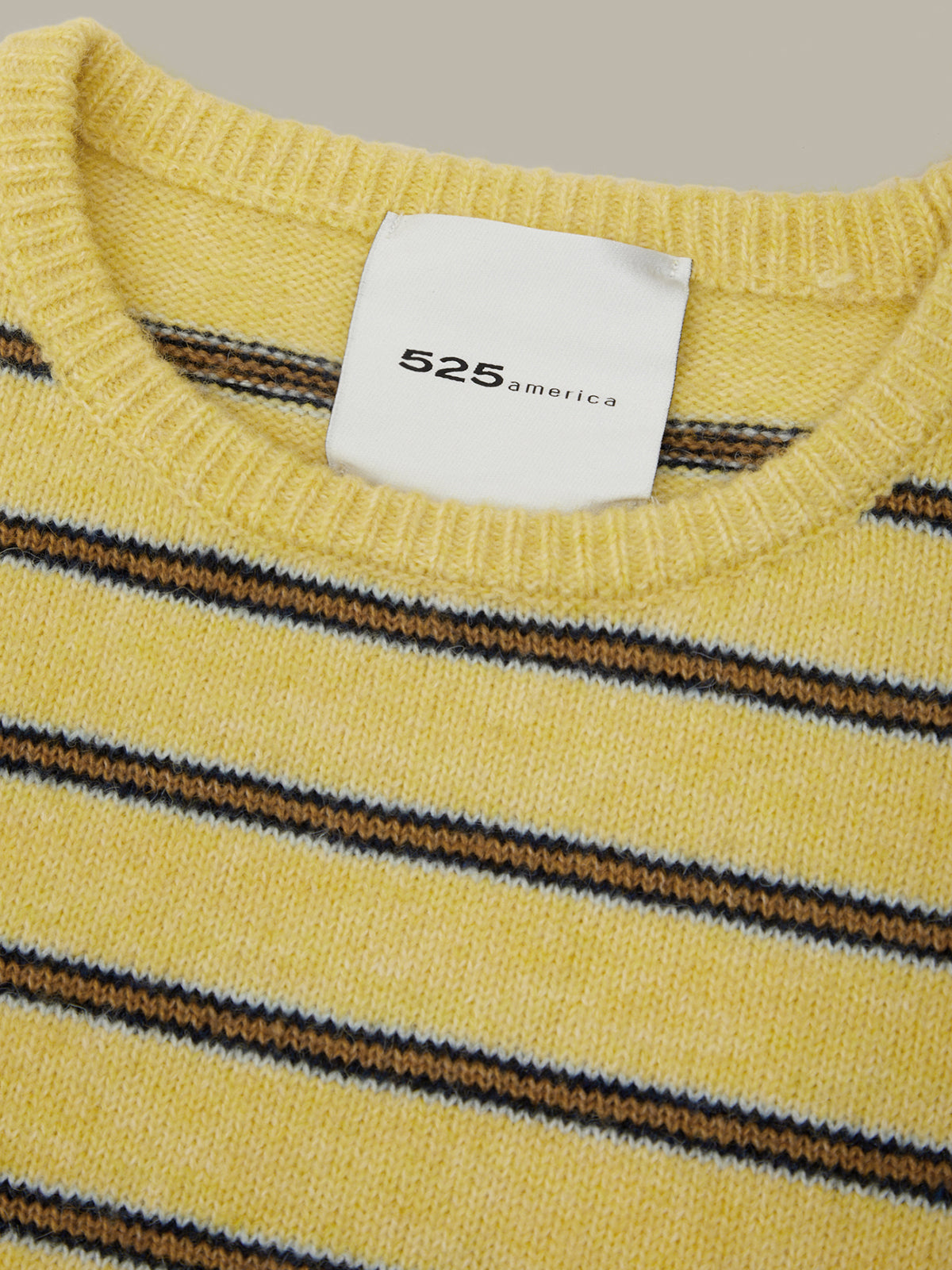 Close-up of a yellow knit sweater with horizontal brown and navy stripes, featuring a white neck label that reads '525 america'.