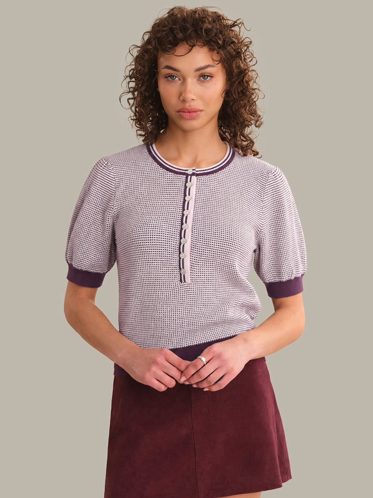 Woman wearing a patterned top and maroon skirt against a plain background