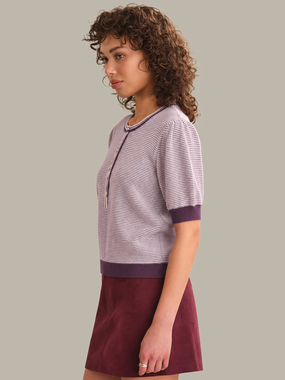 Woman wearing a patterned top and maroon skirt on a plain background