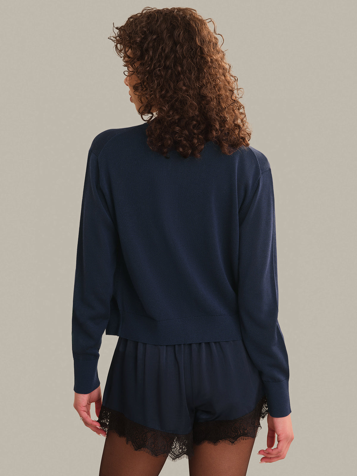 Person wearing a navy blue long-sleeve cardigan and shorts with lace trim on a plain background
