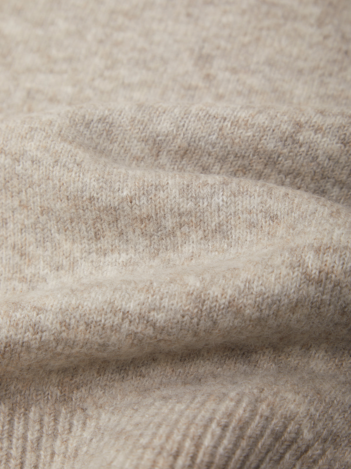 Close-up of a soft knit fabric in a warm light beige or oatmeal tone, showing the texture and weave with gentle folds.