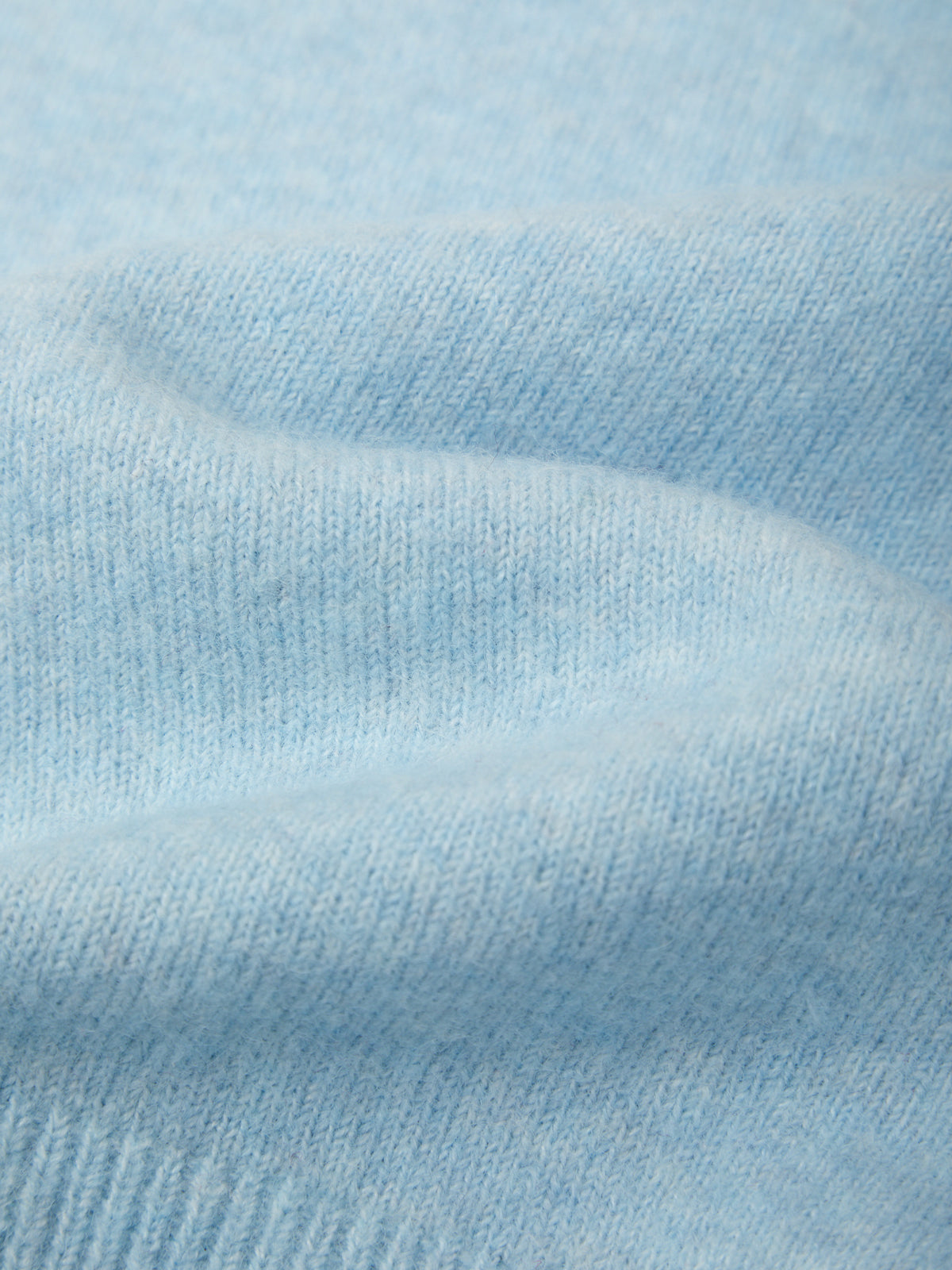A close-up of light blue knit fabric with soft folds and visible ribbed texture.
