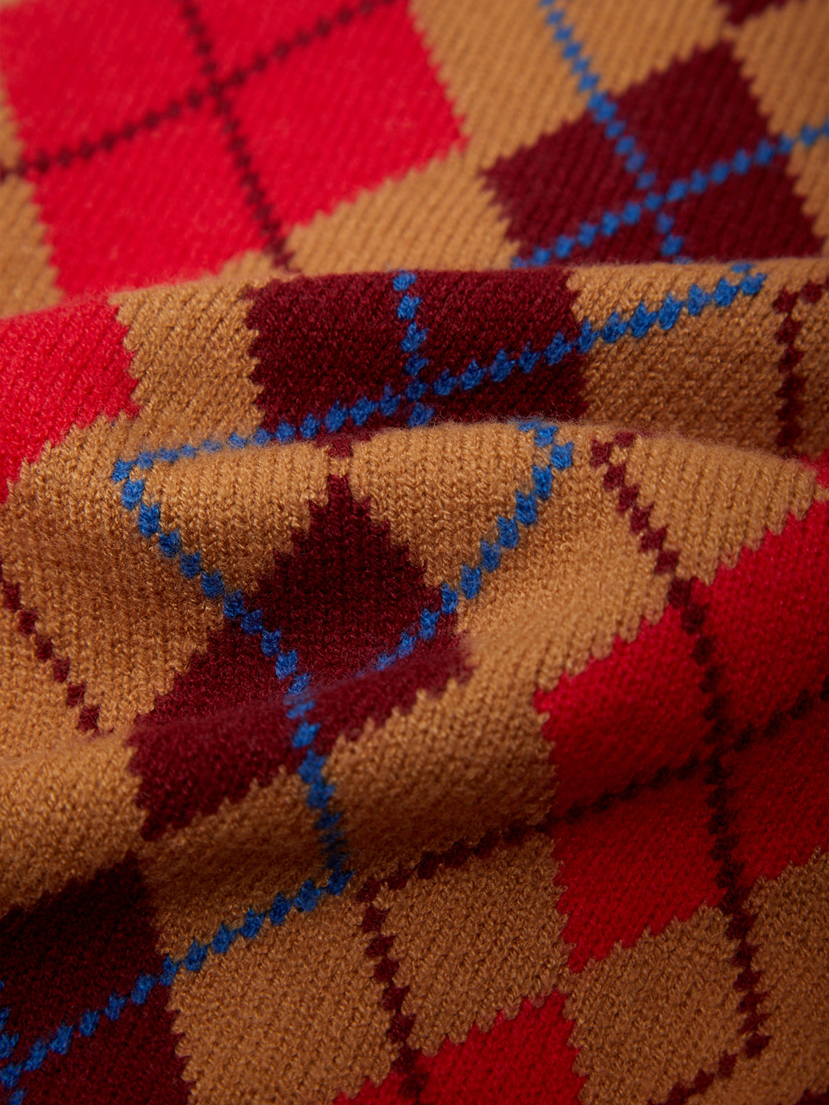A close-up of a knitted fabric with an argyle pattern in tan, red, burgundy, and blue.