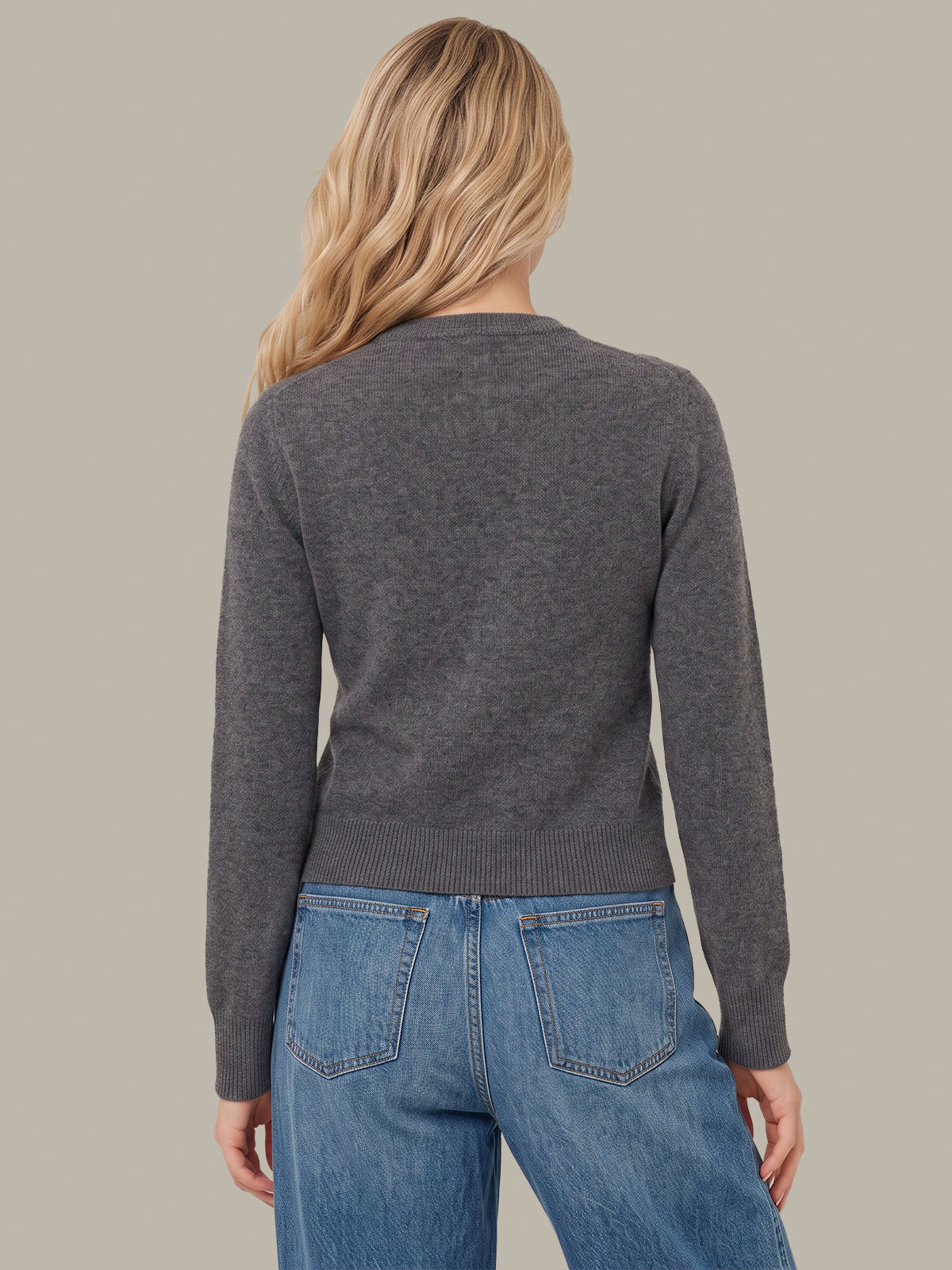 A woman shown from the back wearing a dark gray long-sleeve knit sweater and blue jeans against a solid light gray background.