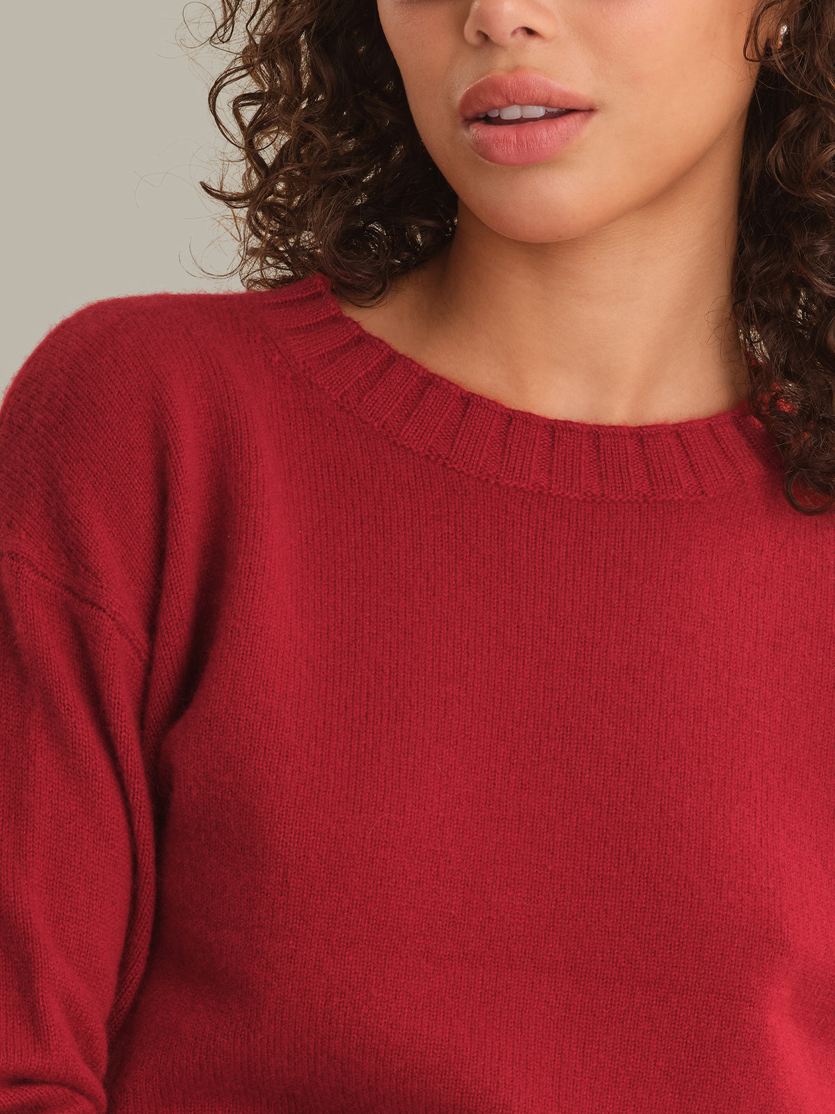 A close-up of a woman wearing a red knit crewneck sweater, showing the texture of the fabric and the ribbed neckline.