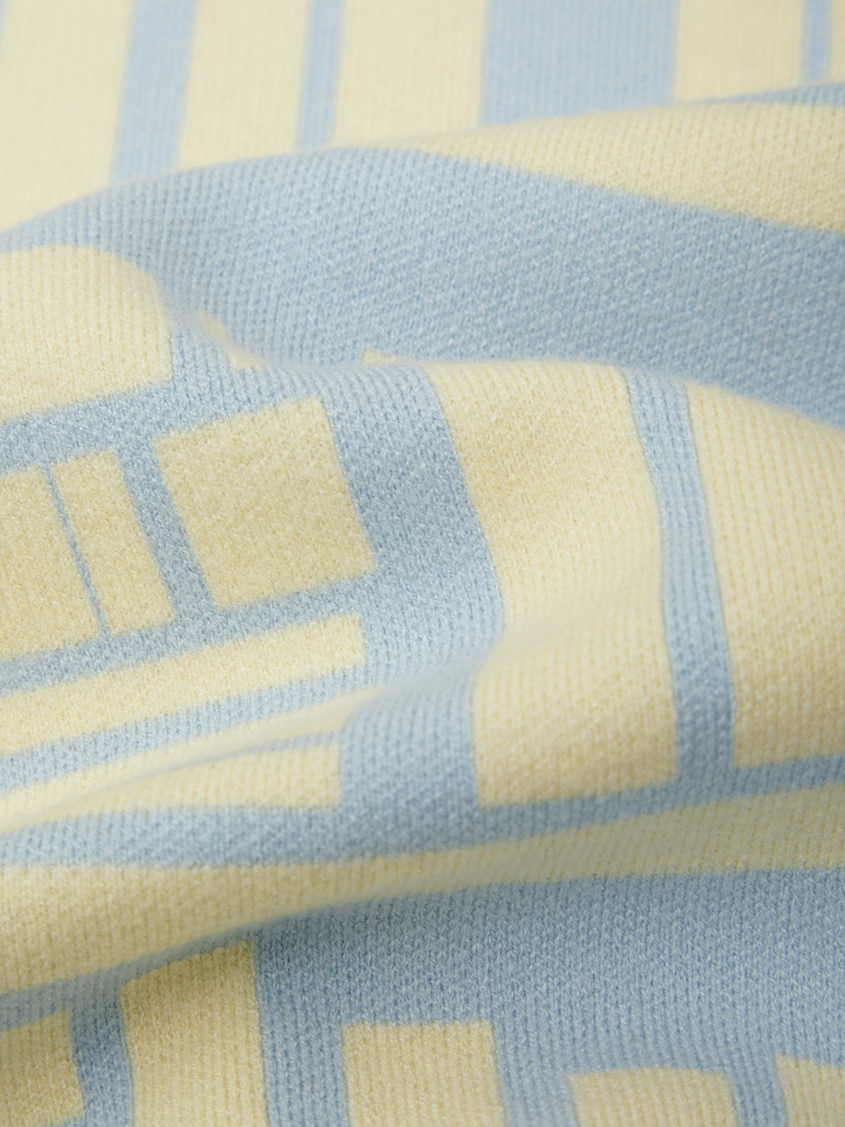 A close-up of a soft knit fabric with a geometric pattern in light blue and pale yellow, showing the texture and folds of the material.