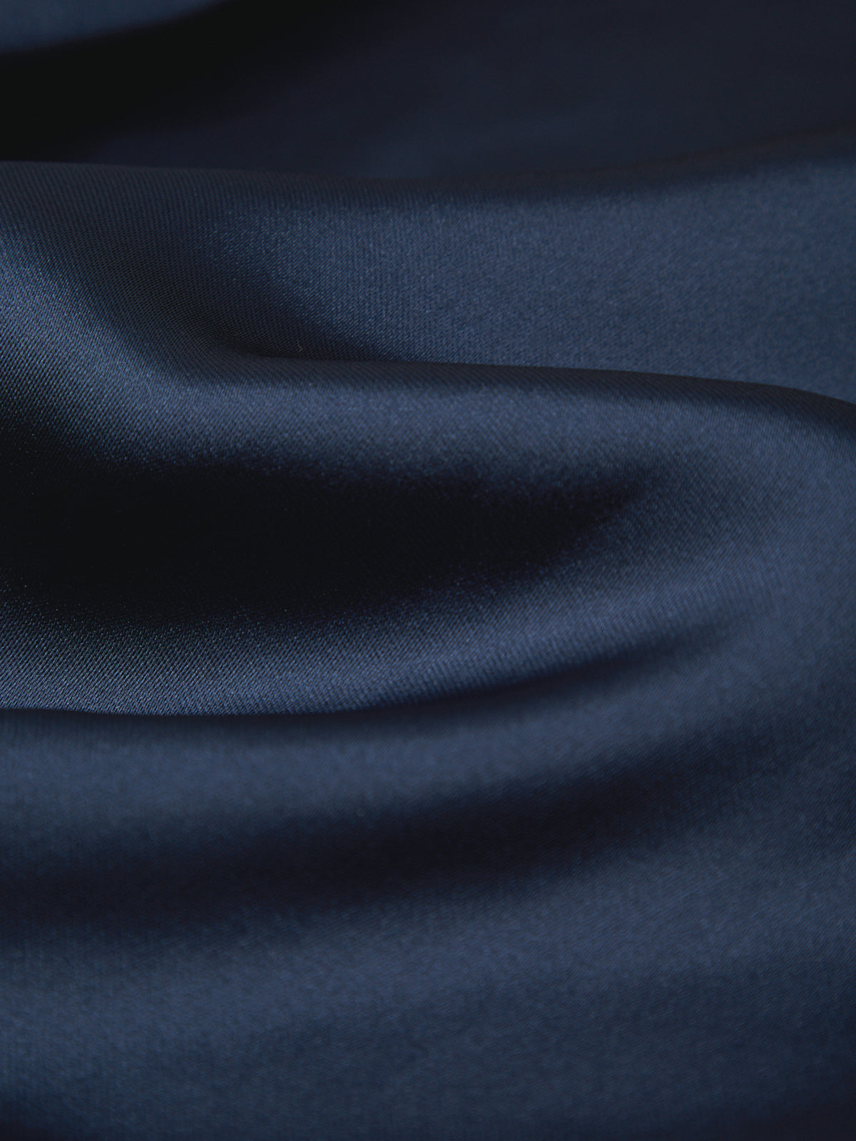A close-up of draped dark navy blue fabric with soft folds and a smooth texture.