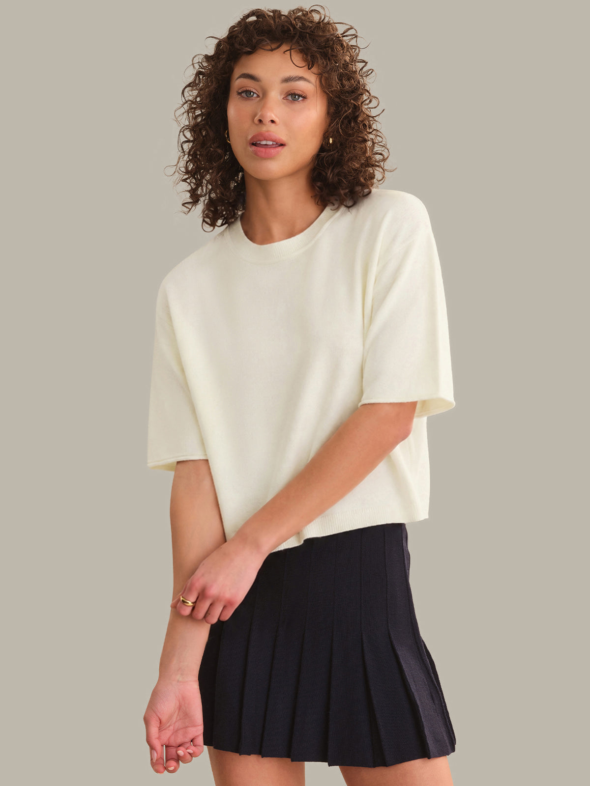 Woman wearing a white oversized shirt and black pleated skirt on a plain background