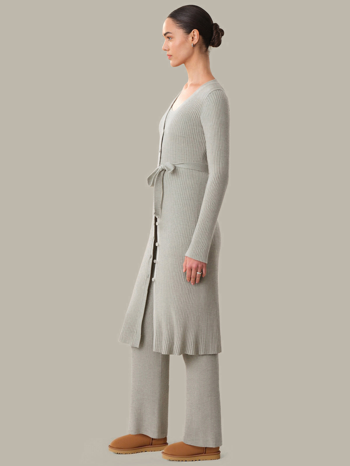 Woman wearing a long light gray cardigan and pants on a neutral background