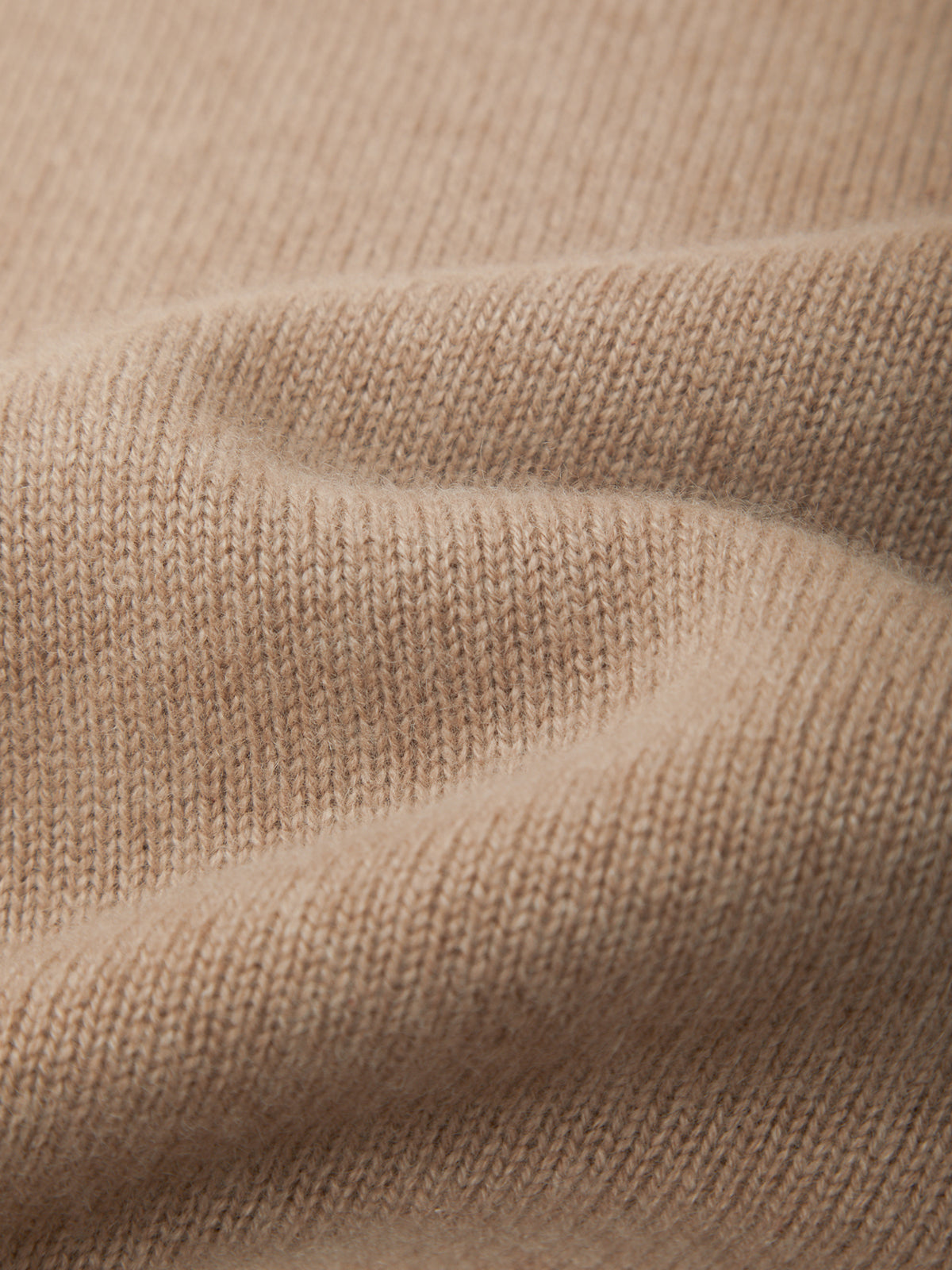 Close-up of a soft knit fabric in a warm light beige or camel color, showing the texture and drape of the material.