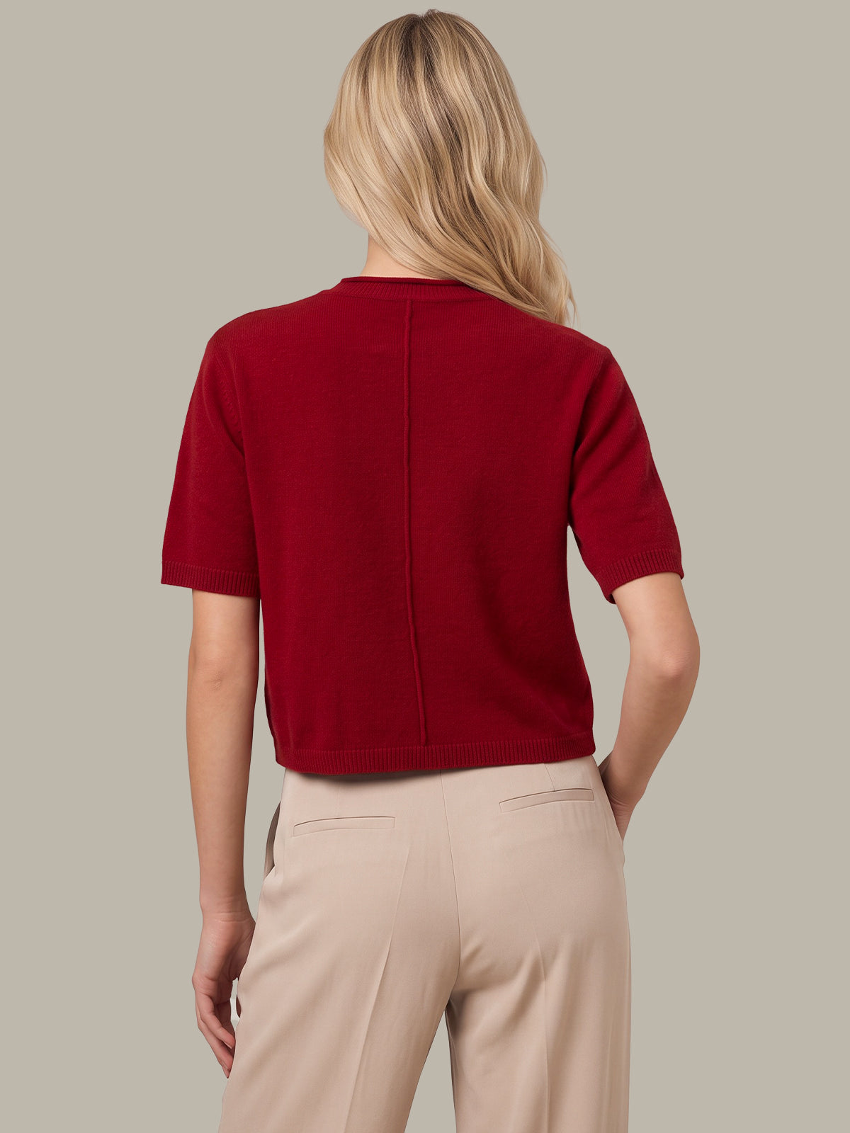 A woman shown from the back wearing a short-sleeve knit top in deep burgundy red and beige trousers, against a solid light gray background.