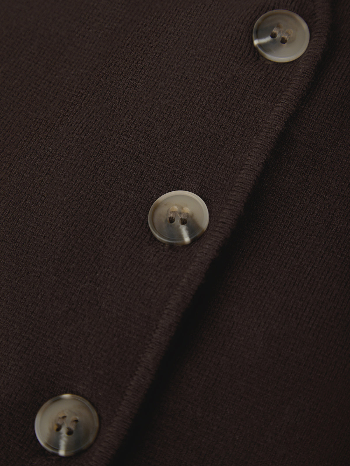 Close-up detail of a dark brown knit garment with three visible round buttons along the front edge.
