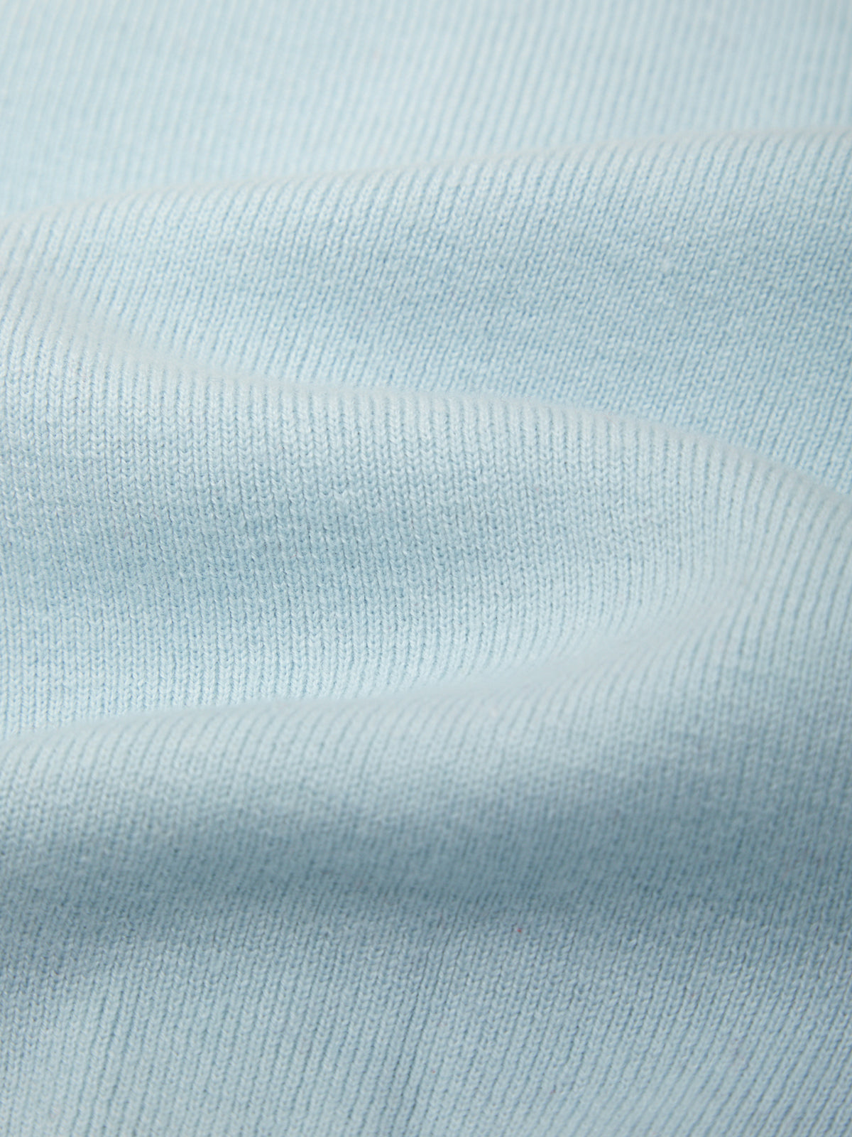 A close-up of light blue ribbed knit fabric with soft folds and a smooth texture.