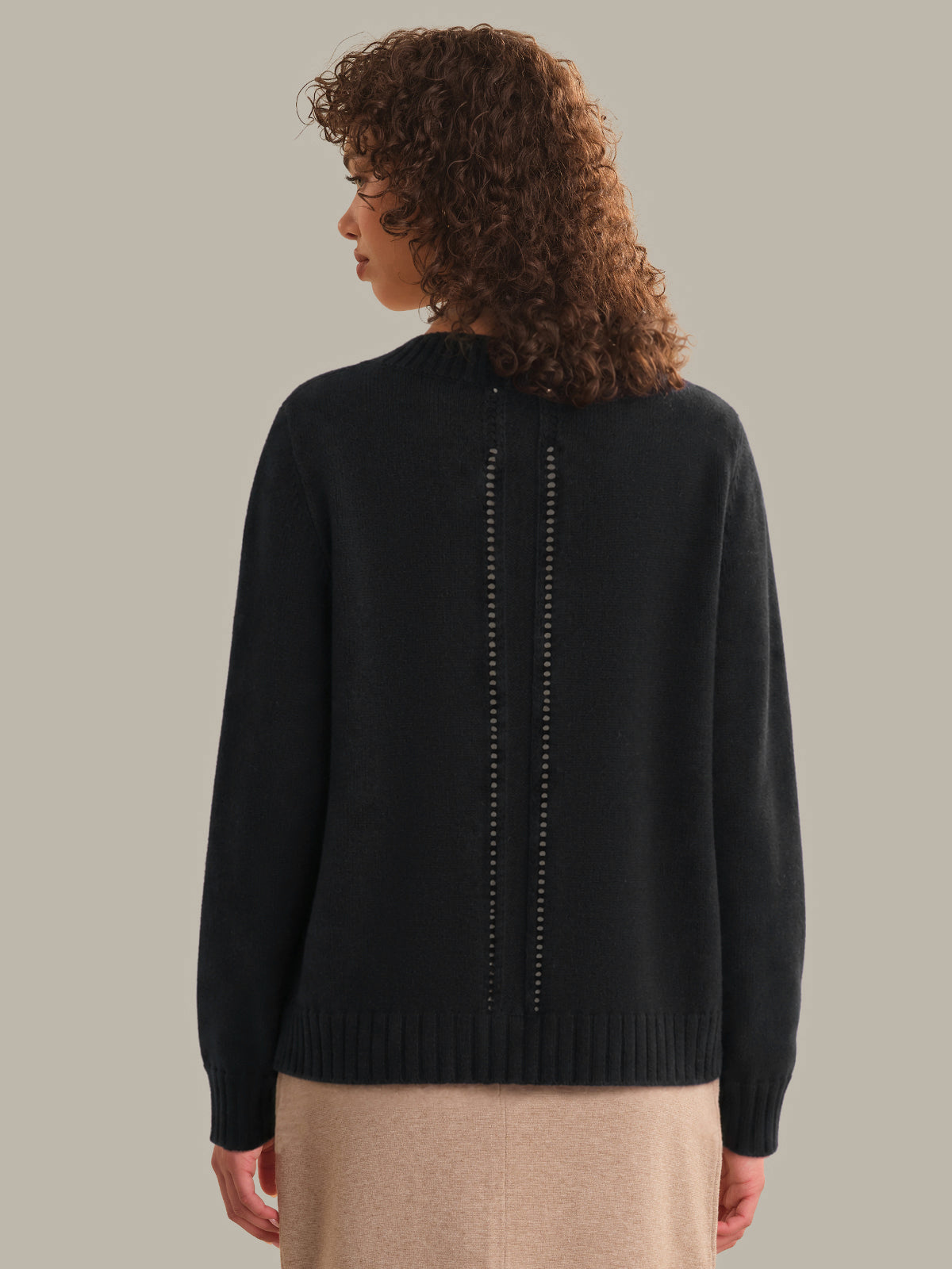 Person wearing a black sweater with decorative back panel on a beige background