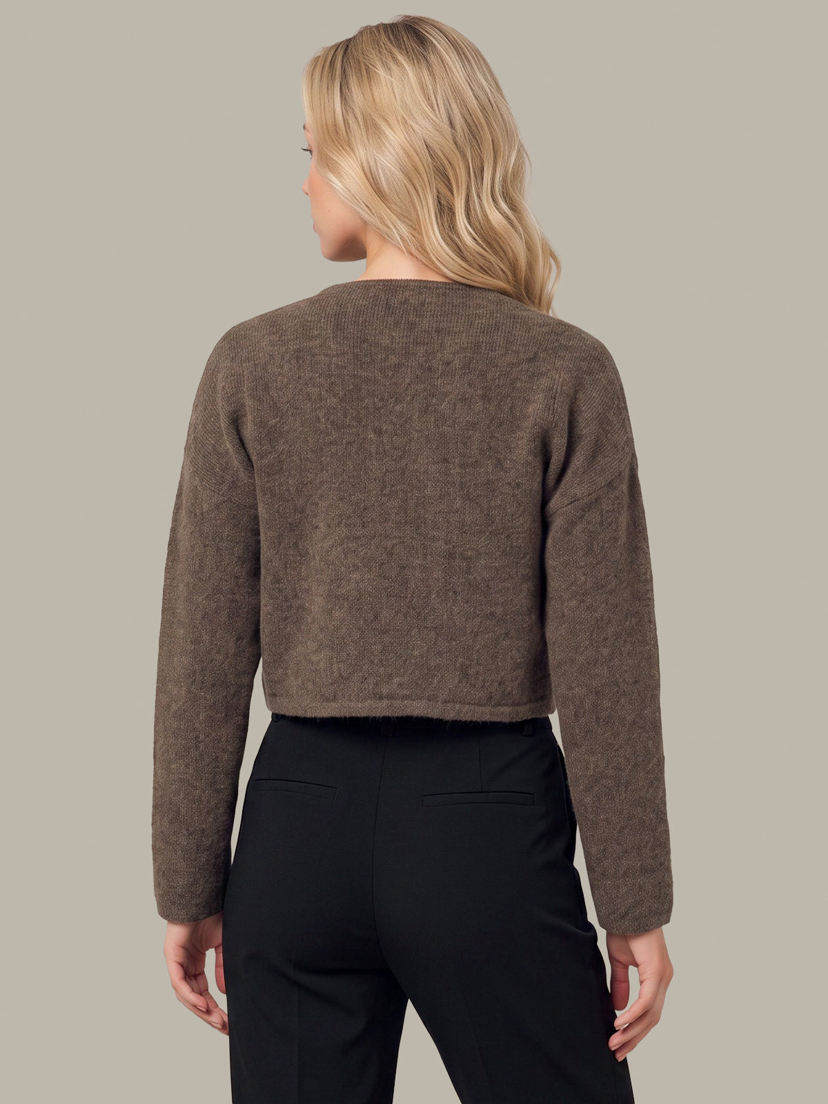 A woman shown from the back wearing a cropped, long-sleeve knit sweater in a heathered taupe-brown color, paired with black trousers, against a solid light gray background.