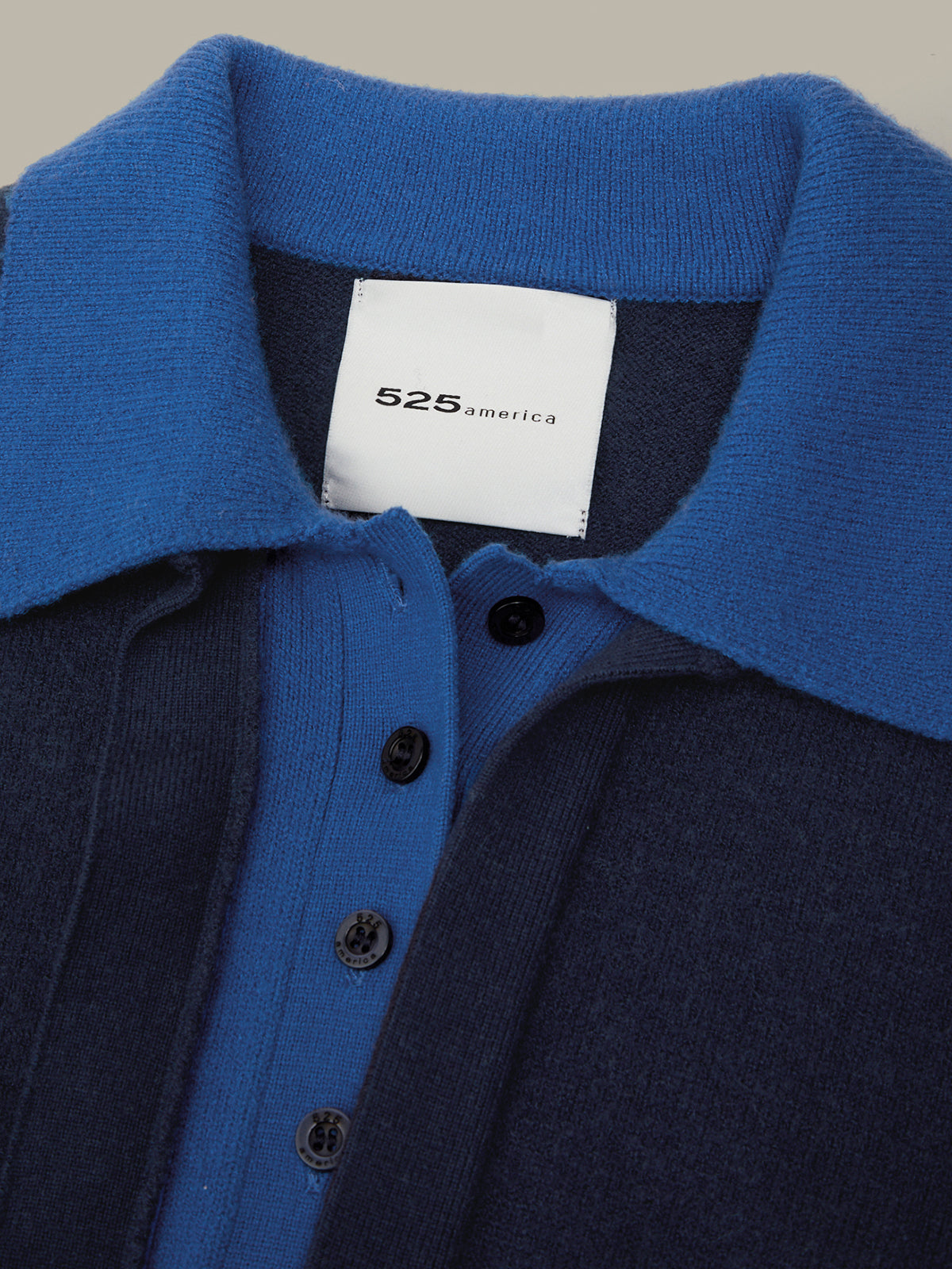 Close-up of a knit polo shirt collar and button placket in two-tone blue and navy, with a white neck label reading 525 america.