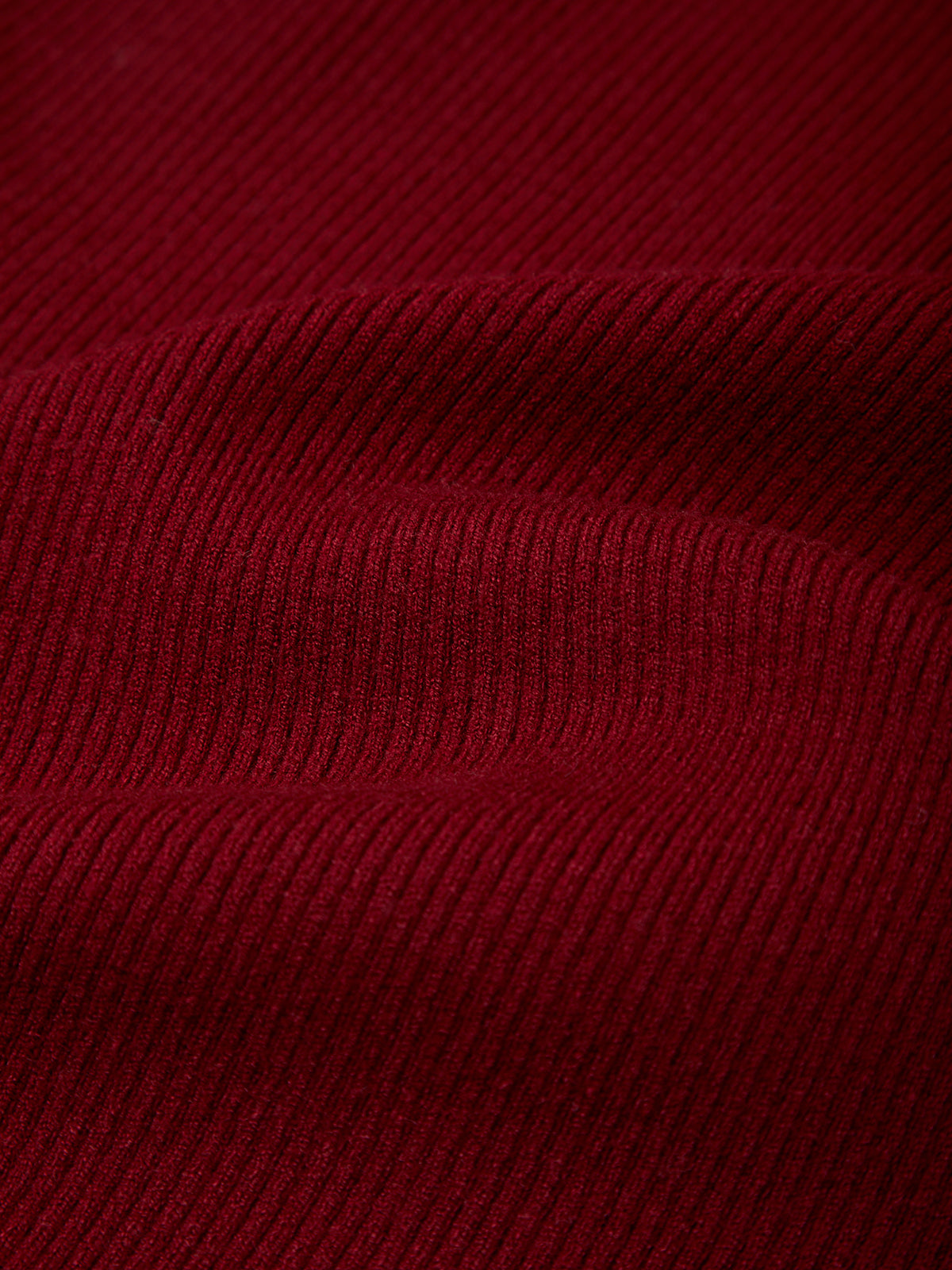 A close-up of dark red ribbed knit fabric with a fine vertical corduroy-like texture and soft folds.